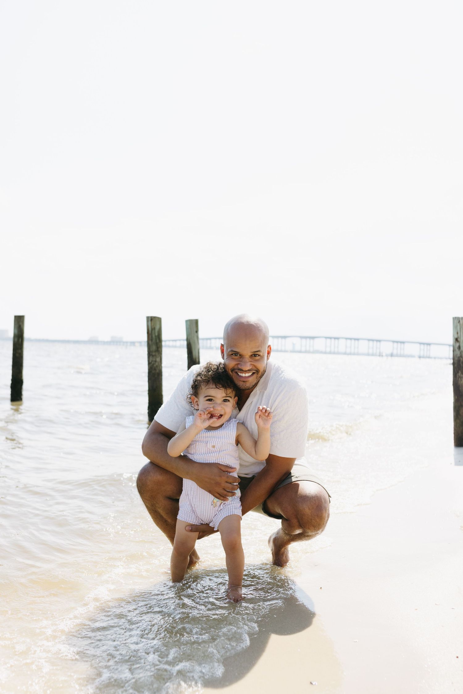 Two people enjoy playful moments at the beach shore while crouching near the water.