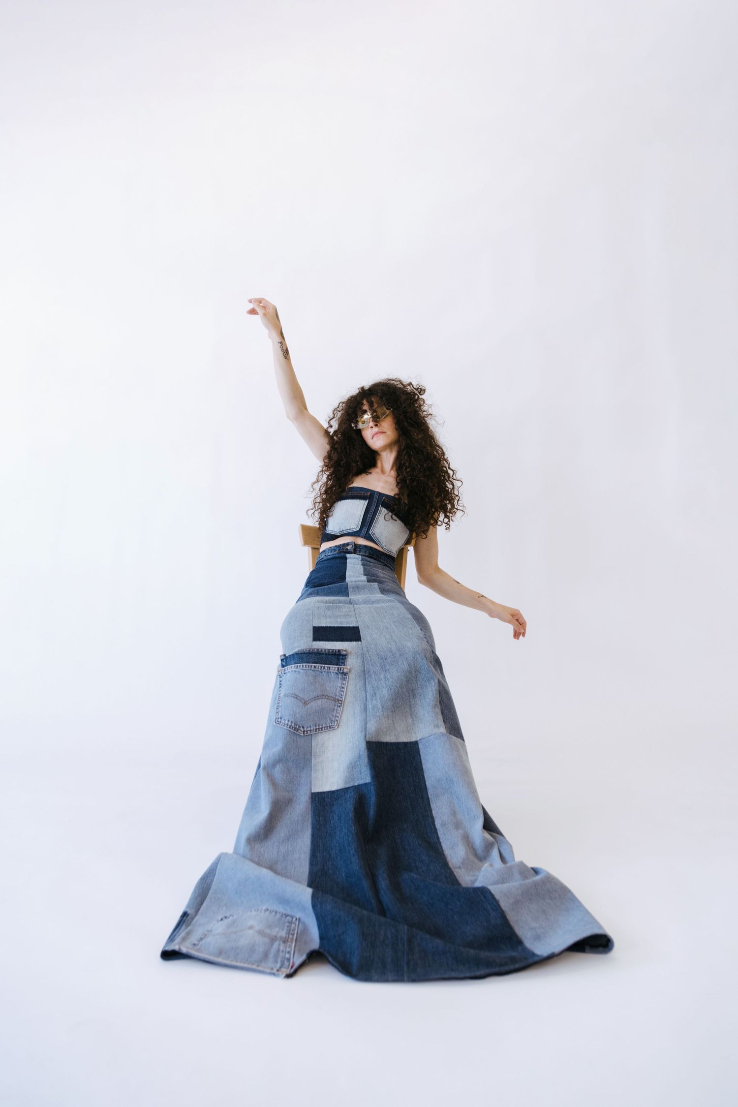 A dancer in a flowing patchwork denim gown poses gracefully against a white background.