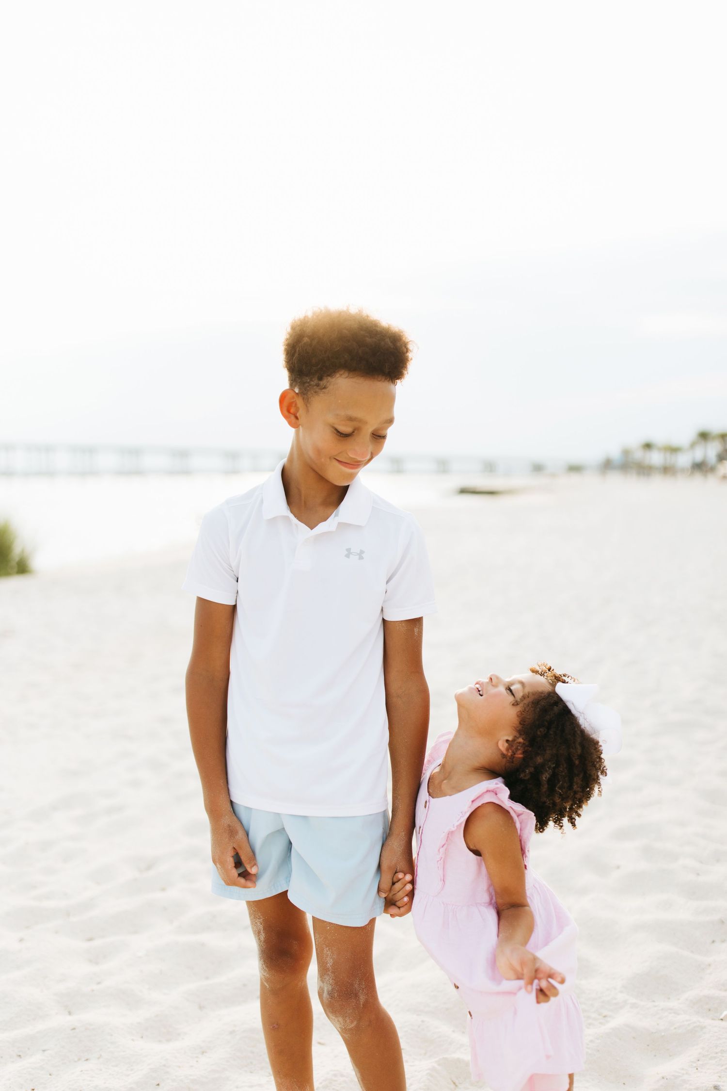 Children in white and pink outfits play joyfully together on a pristine sandy beach.