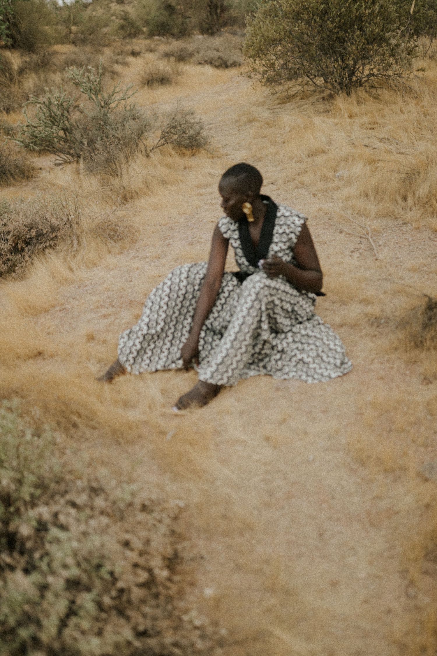 Someone in a polka dot dress lies on dry desert ground while holding a digital camera.
