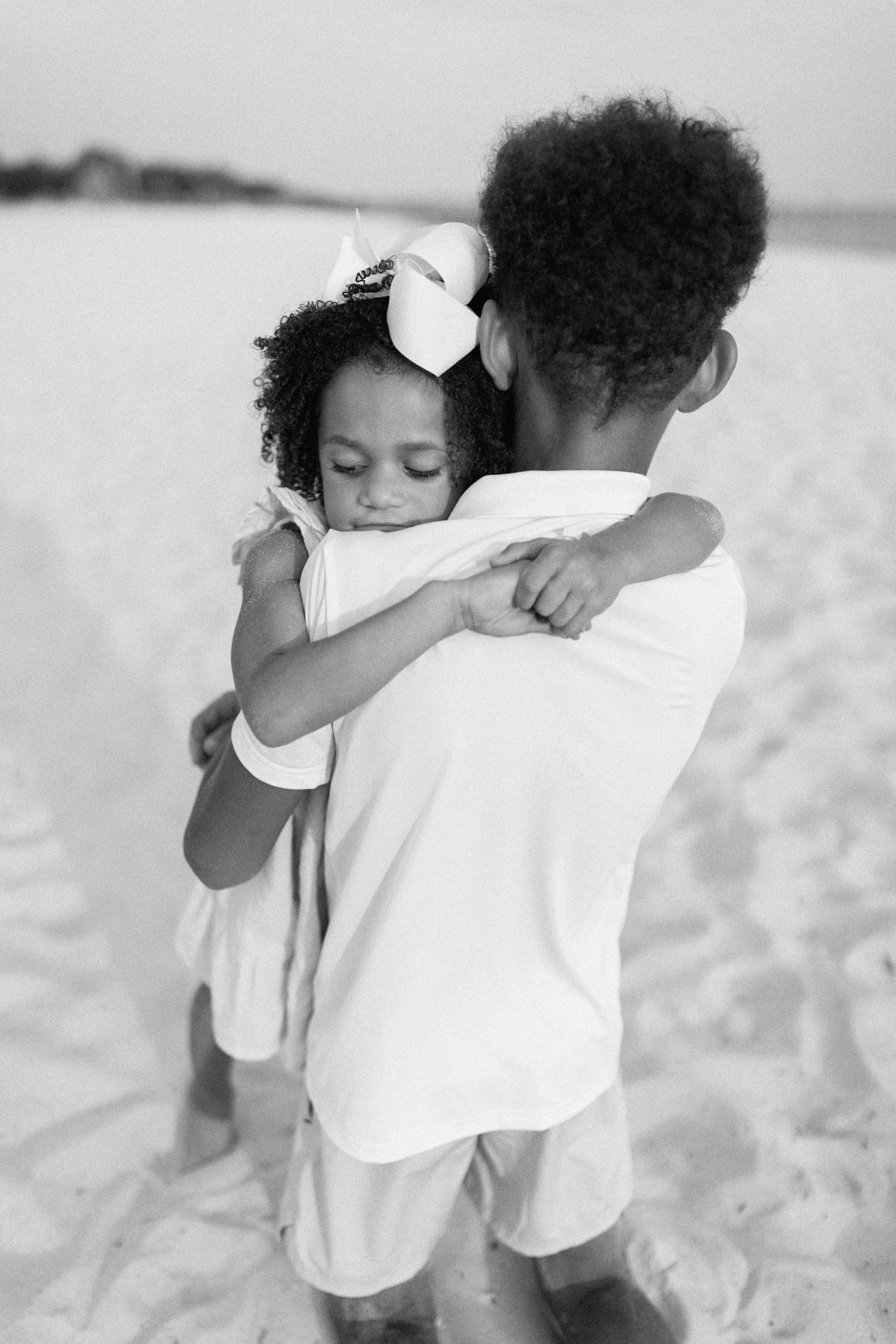 Sweet black and white photo series of siblings hugging on beach.
