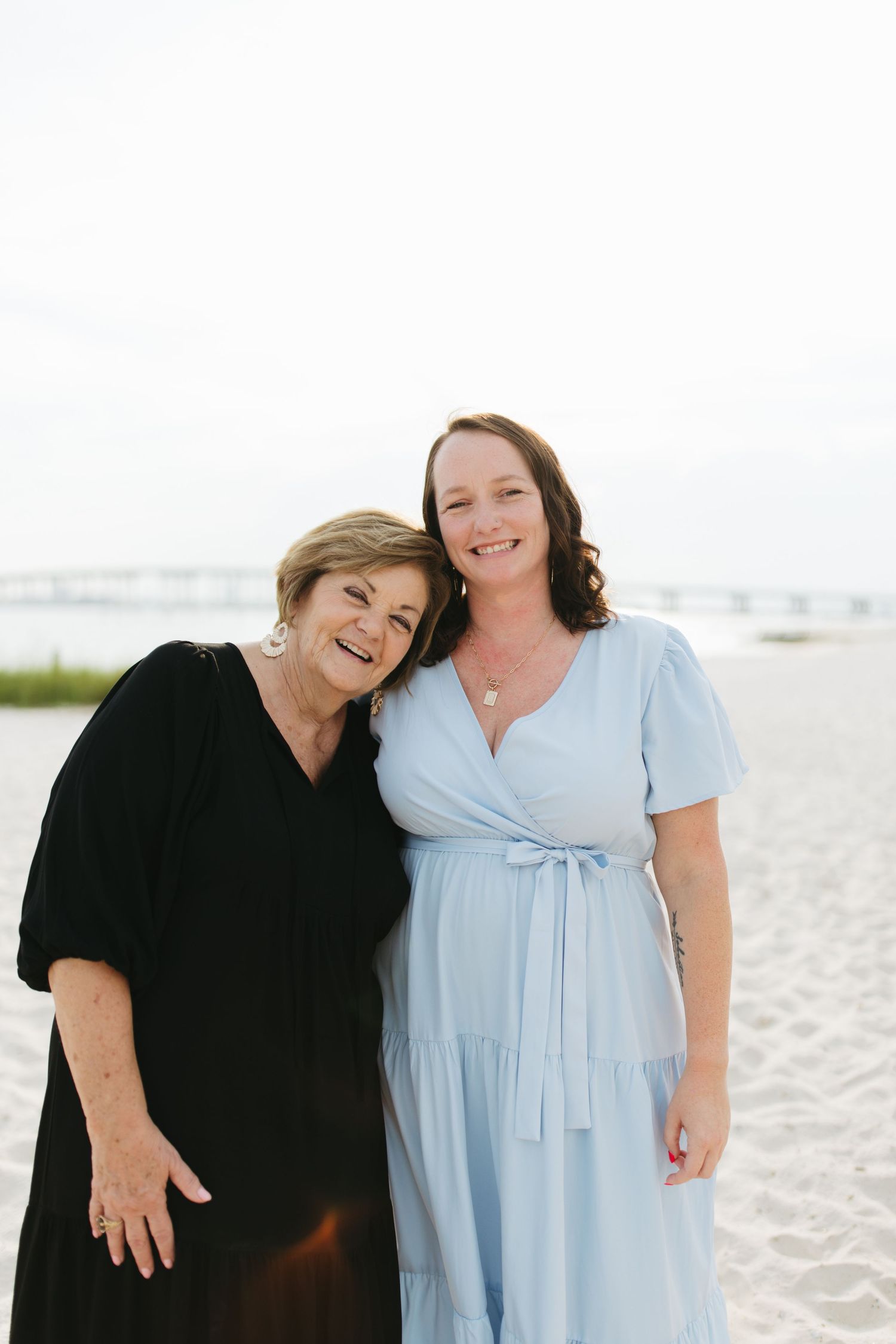 Two people wearing contrasting black and light blue outfits share joyful moments together on a bright sandy beach.
