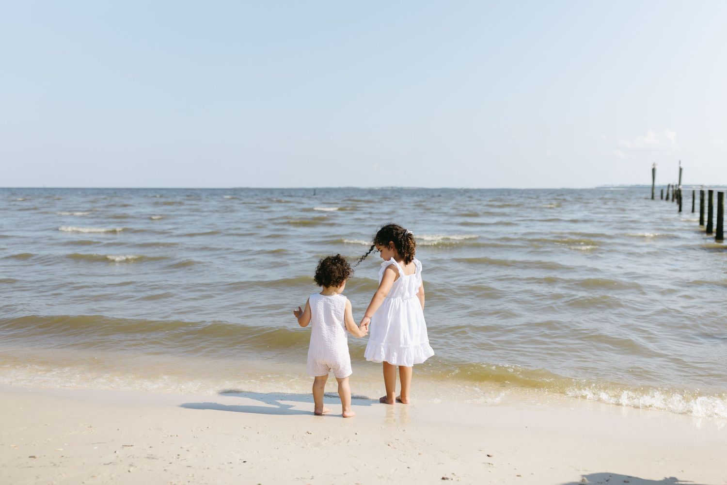 Two people dressed in white outfits explore a sandy beach together on a bright sunny day.
