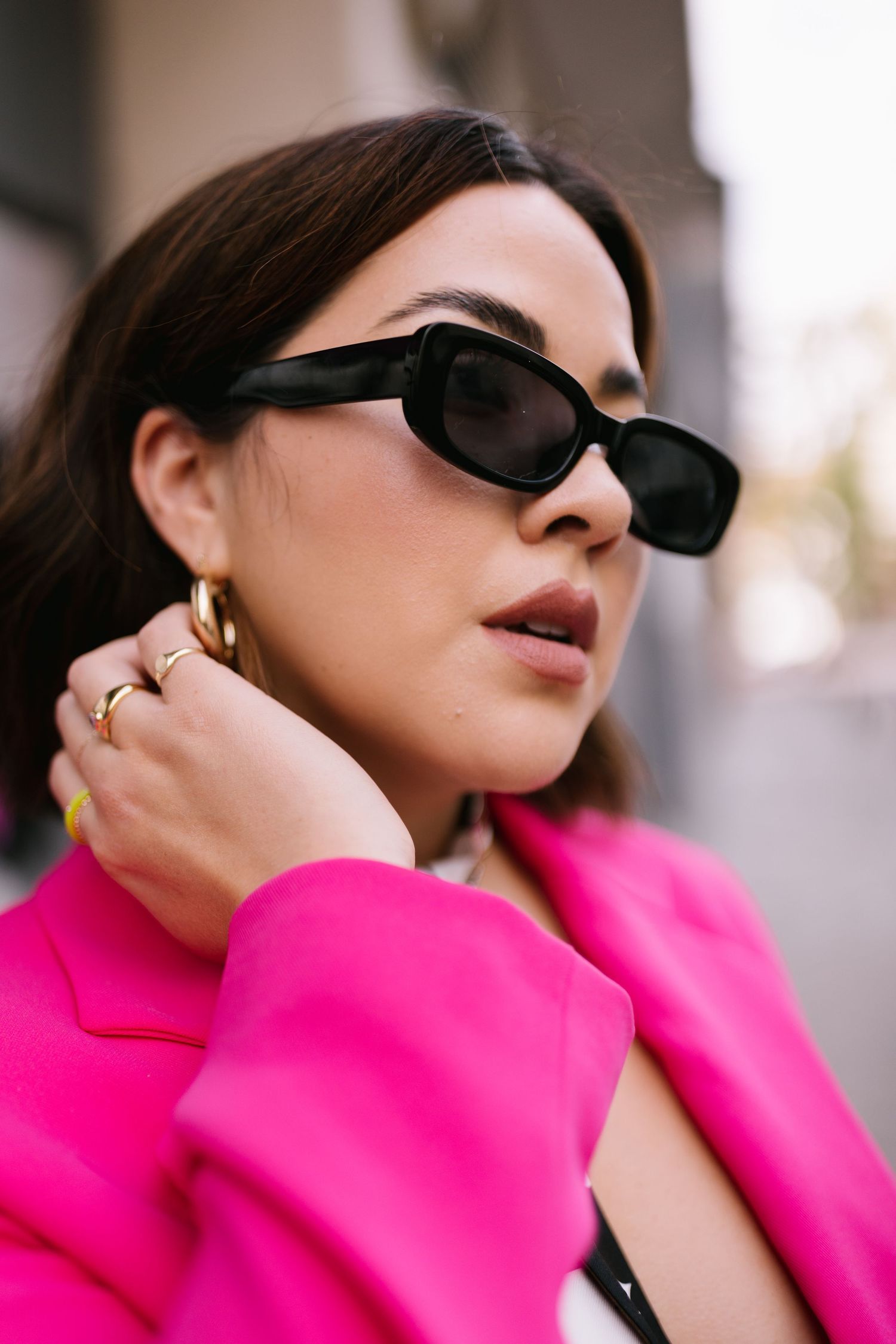 Portrait in bright pink blazer with black sunglasses and gold hoop earrings, styled for modern fashion photography.