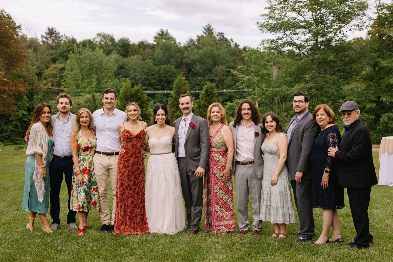 A panoramic series of group photographs taken outdoors showing wedding guests arranged in casual poses on a grassy meadow.