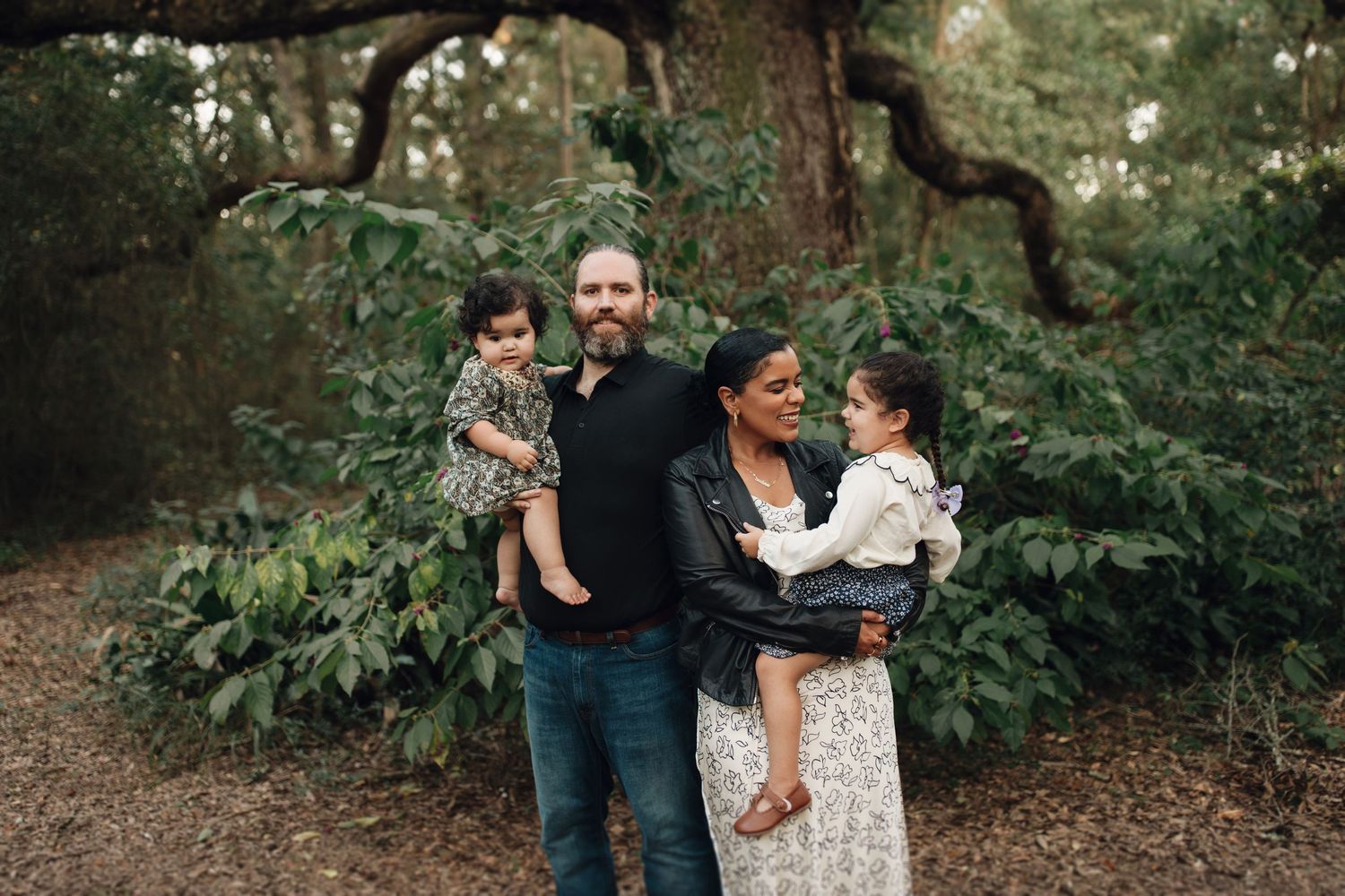A group of people embrace while standing in a lush wooded area with green foliage in the background.