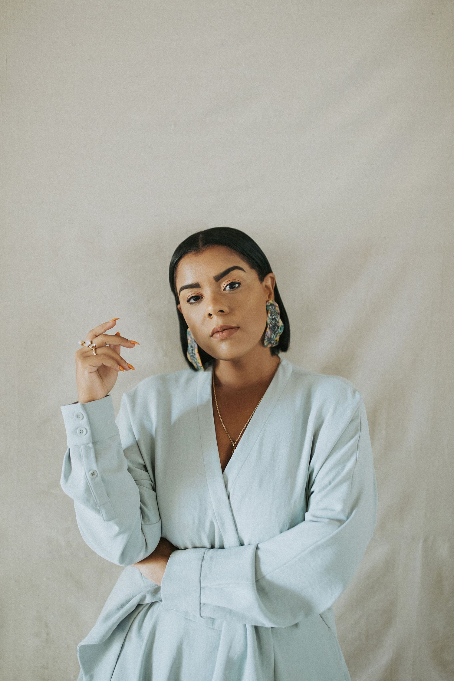 Portrait of someone in a light blue blazer dress with statement earrings against a neutral background.