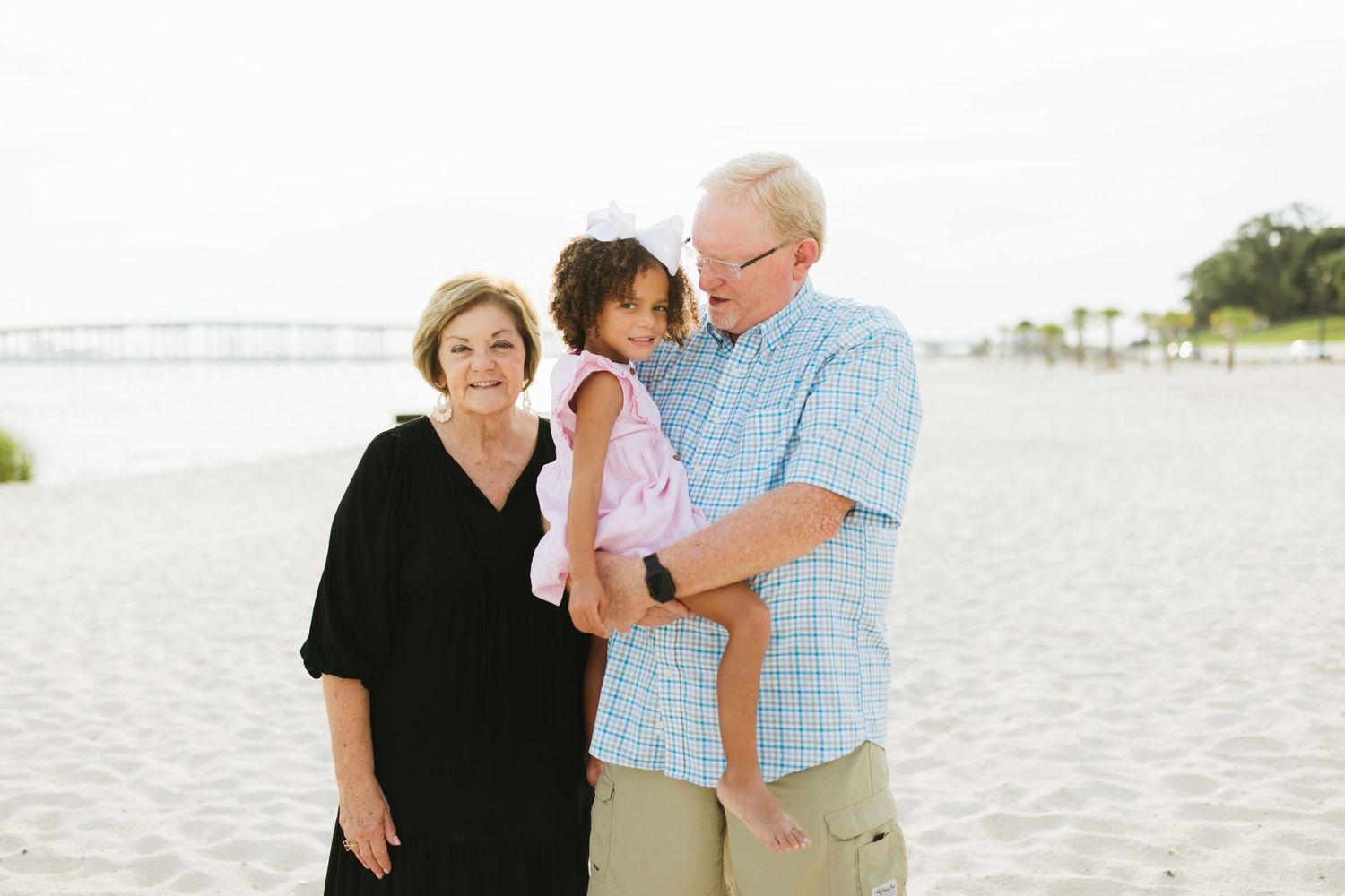 A family enjoys a candid moment together while walking on a sunny white sand beach.
