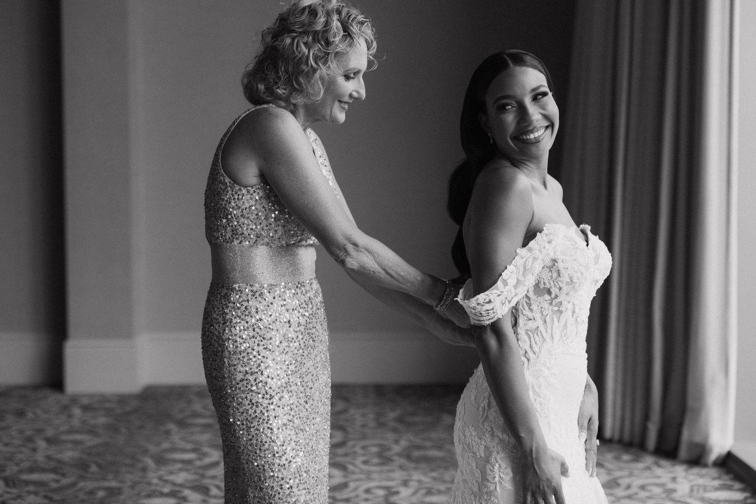 A tender moment in black and white as a mother helps her daughter with final adjustments to a wedding dress.