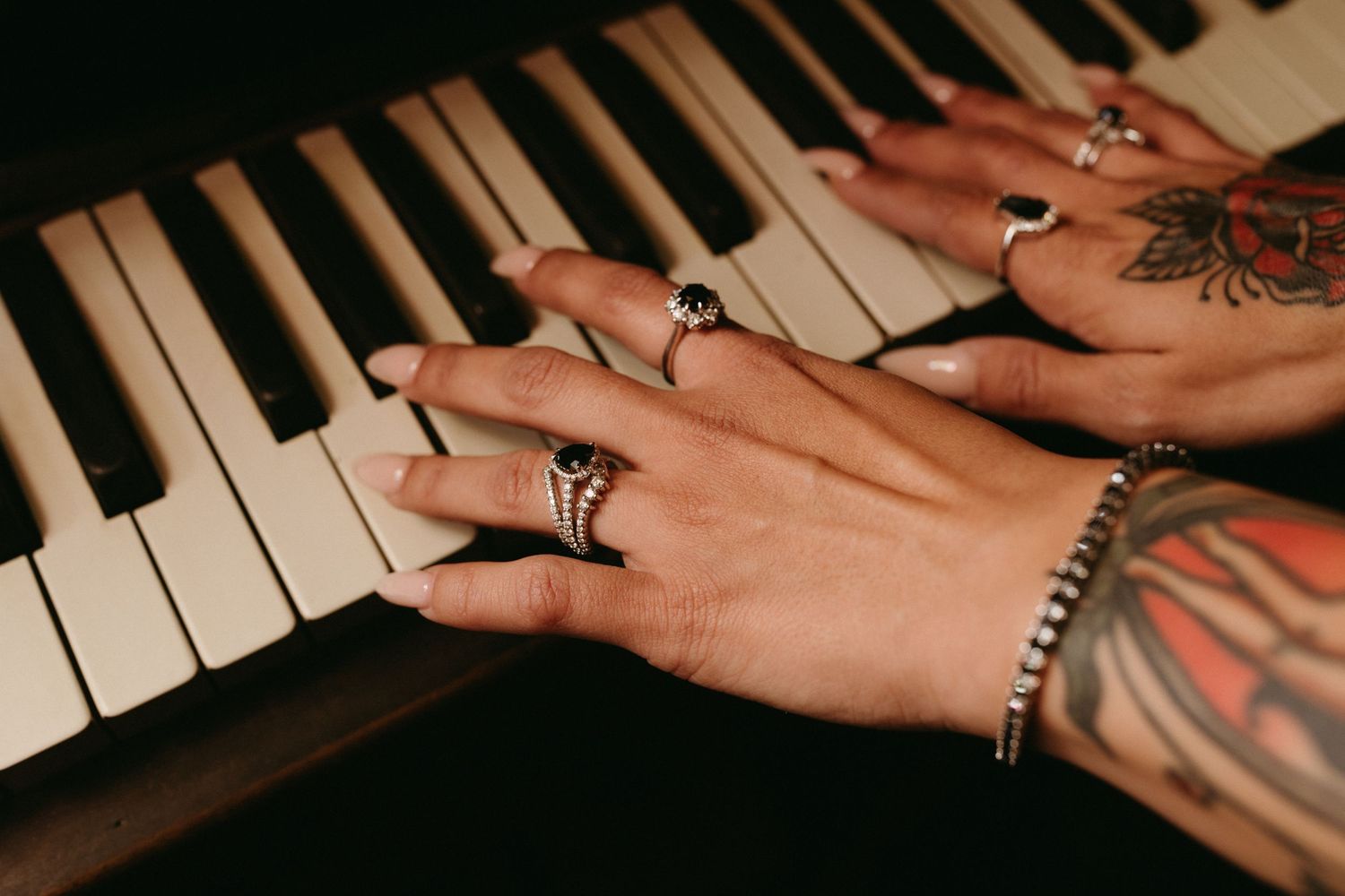 Hands with rings play piano keys in a close-up shot showing fingers on black and white piano keys.
