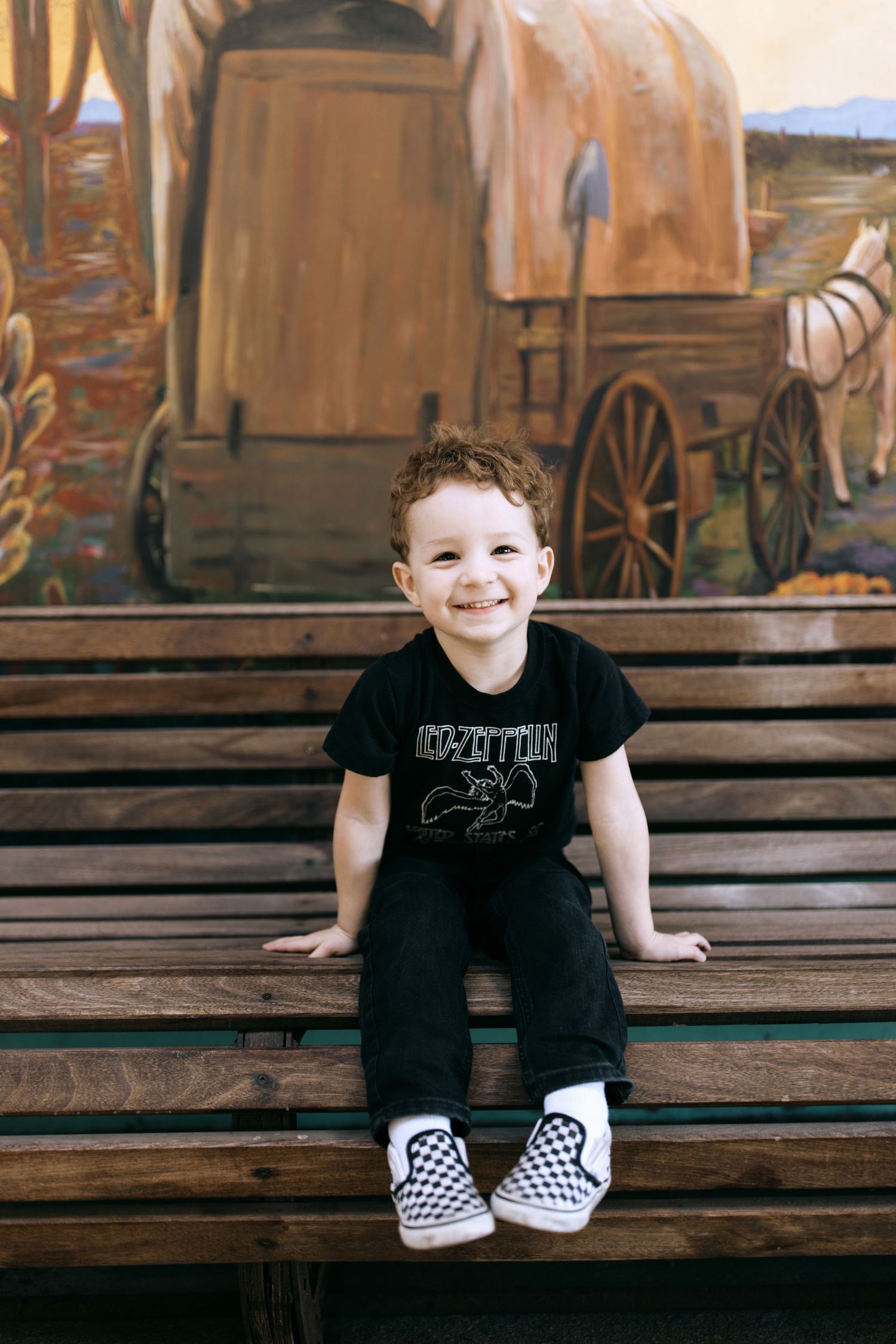 Child in black outfit sitting on wooden steps with vintage wagon mural backdrop.
