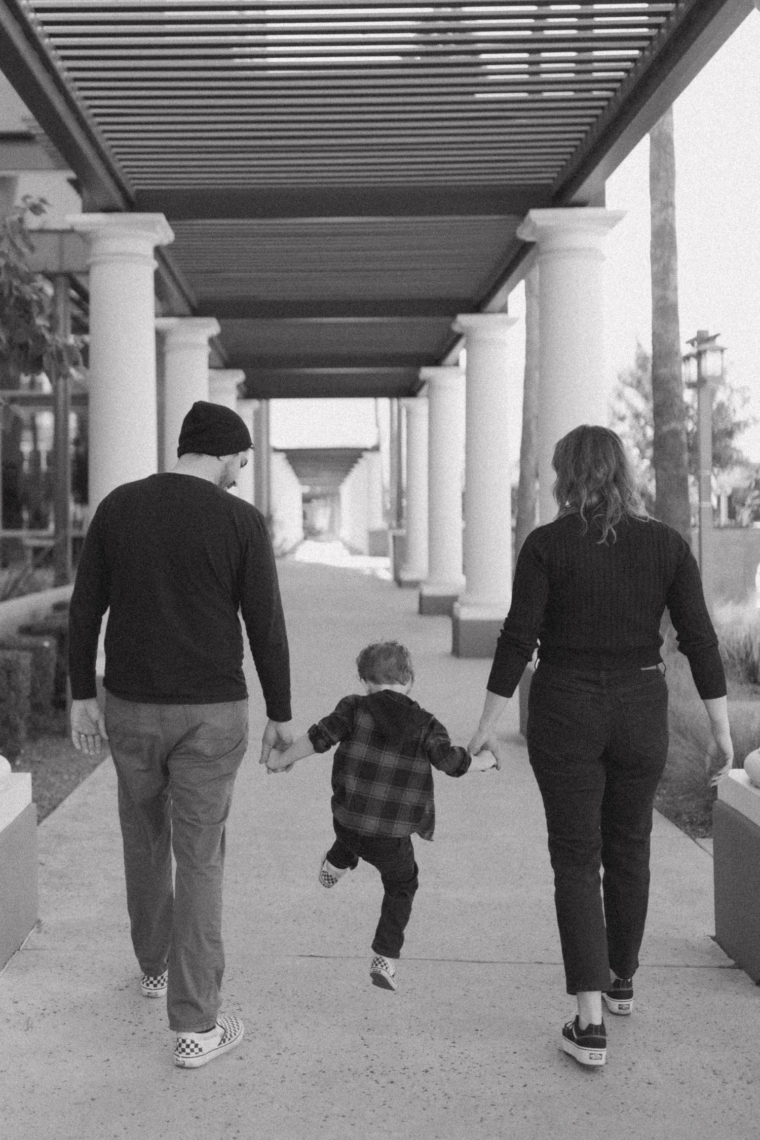 A black and white photograph showing a family walking together under a covered walkway with white columns.