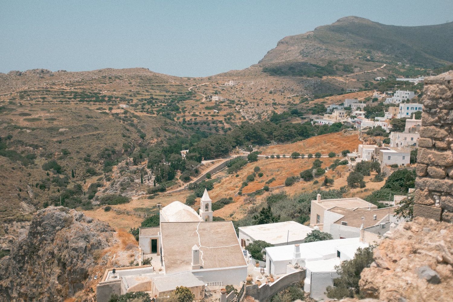 A scenic panoramic view of a traditional Greek village with white buildings nestled in rocky hillsides and mountains.