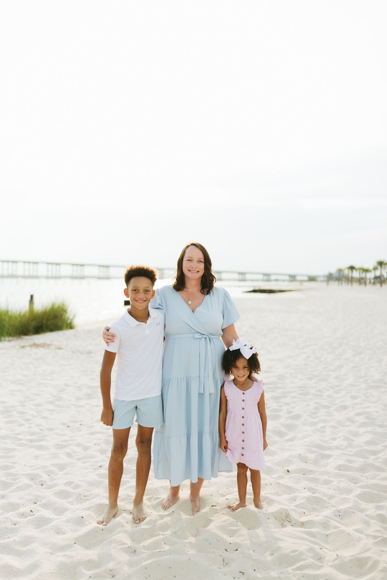 Family members wearing coordinated light blue and white outfits pose together on a sunny beach.