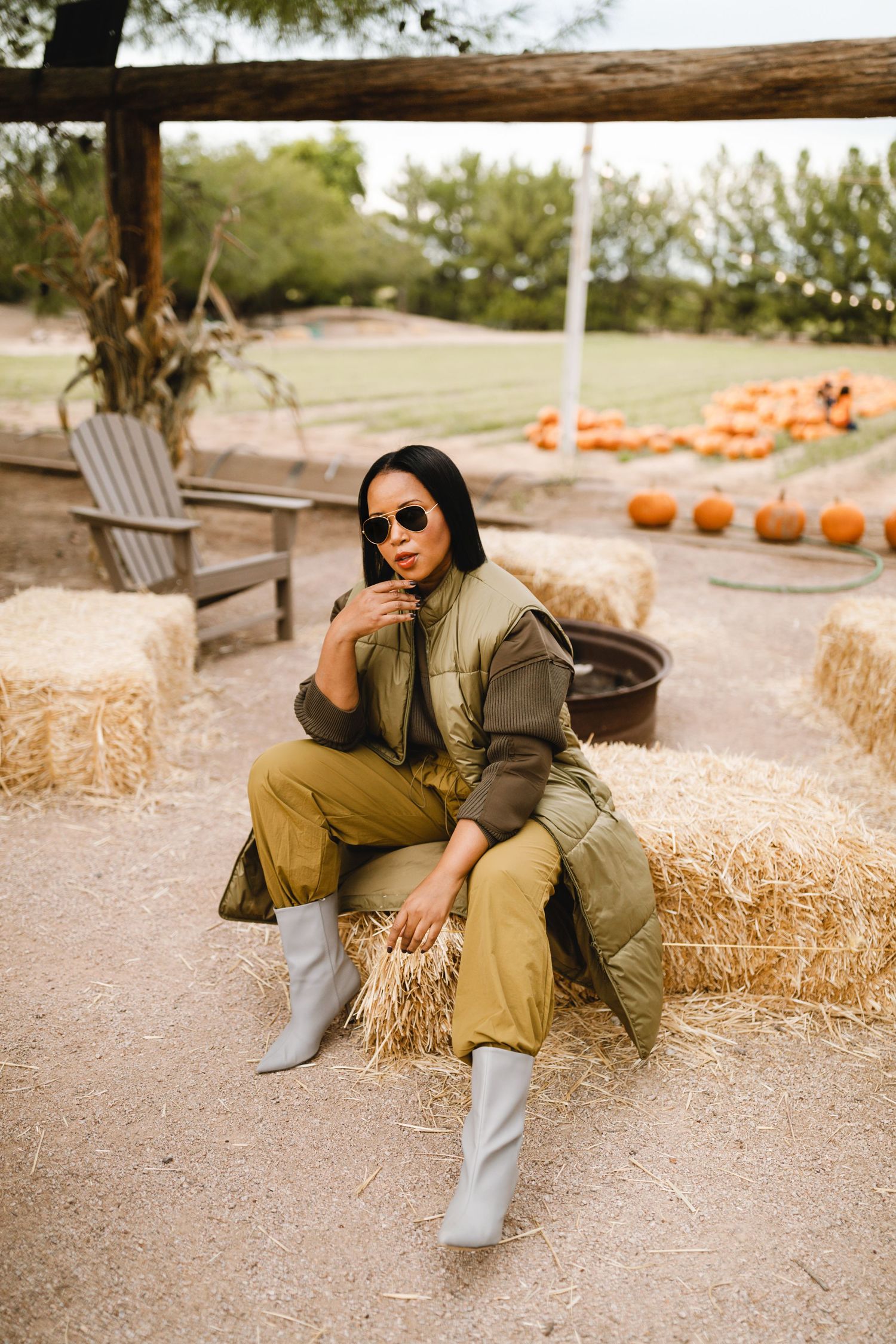 Stylish fall outfit with olive jacket and light jeans photographed at pumpkin patch with hay bales on cool autumn day.