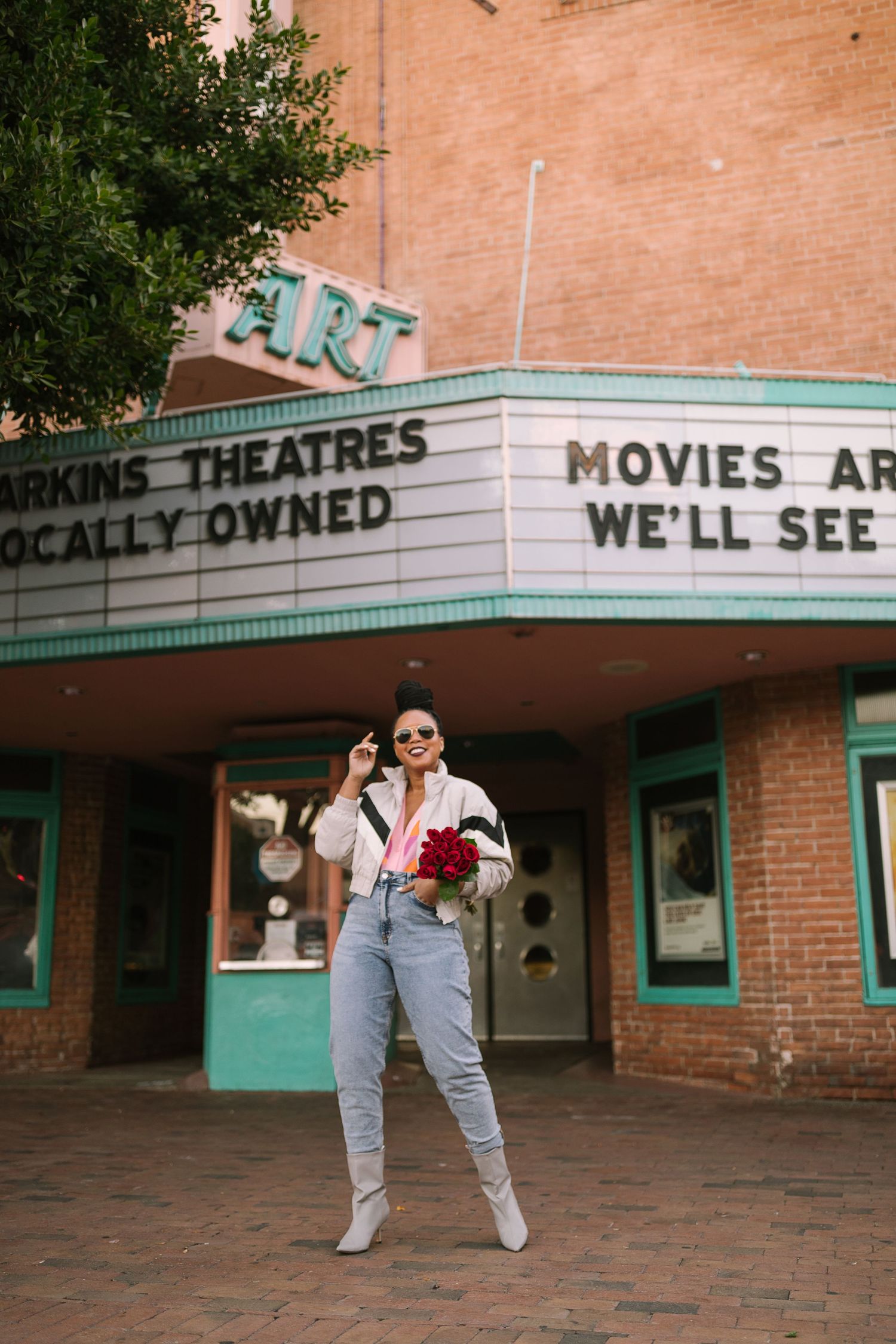 A retro movie theater exterior with turquoise Art Deco trim and vintage signage showing partial text on a brick facade.