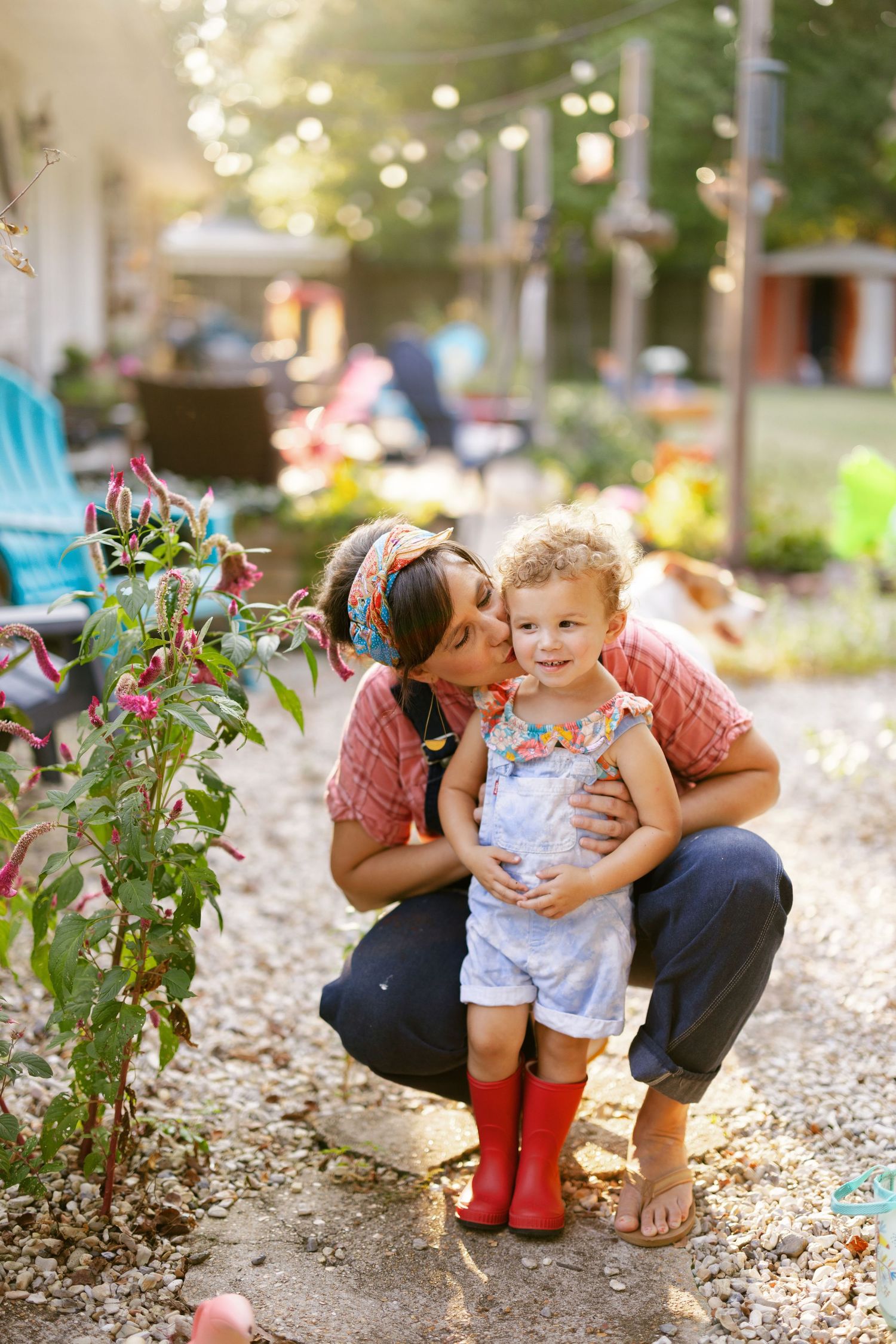 Family shares tender moments outdoors among flowering plants on a sunny summer day.
