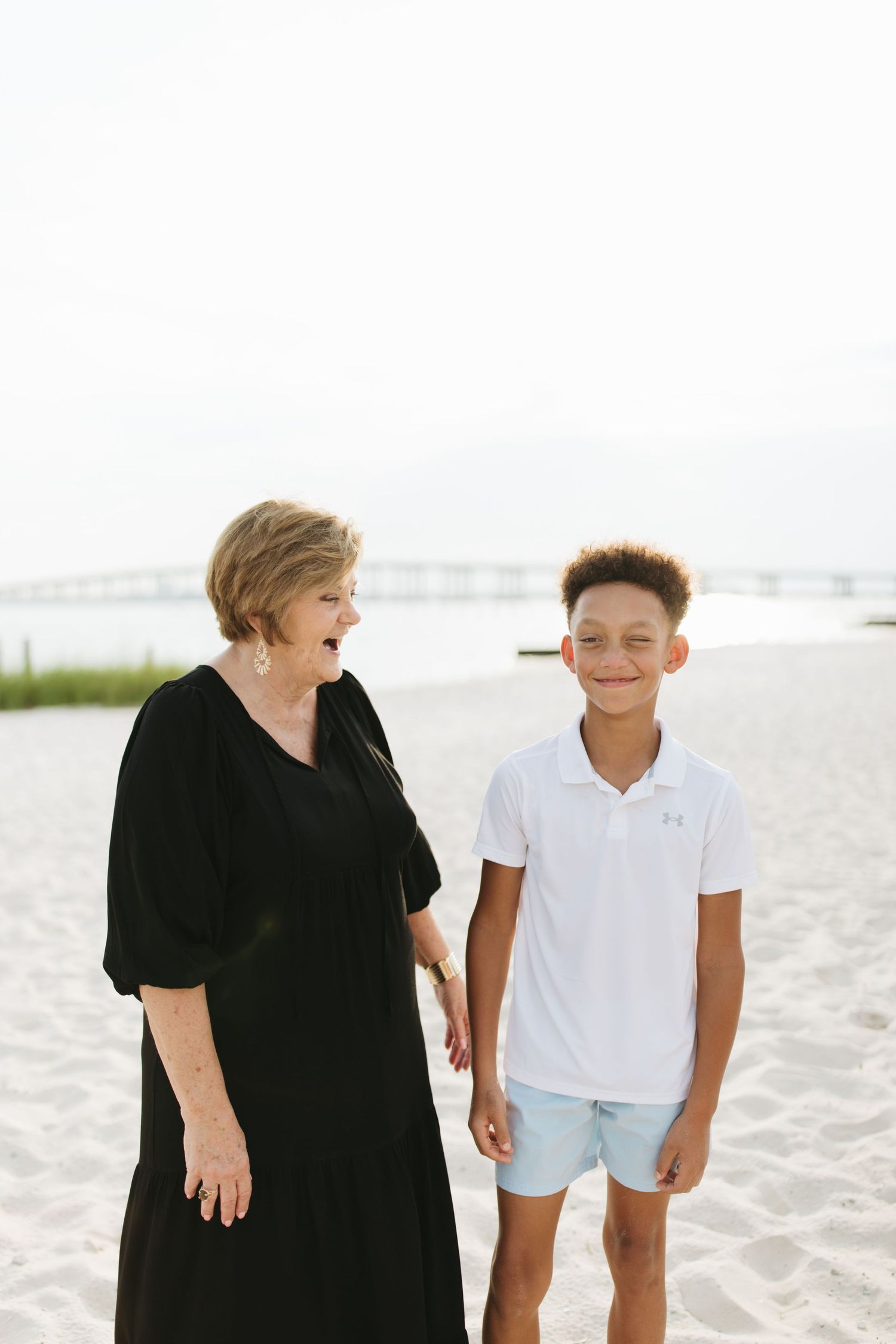 Two people share joyful moments while walking together on a bright sandy beach wearing black and white outfits.