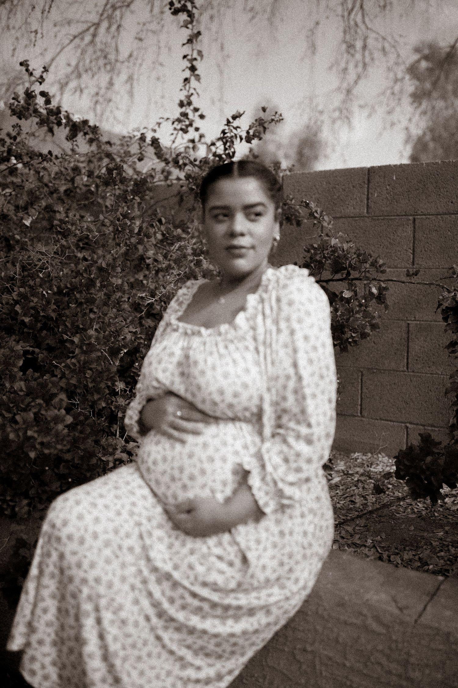 A series of black and white photos showing a person in a polka dot dress sitting and posing outdoors by a garden wall.