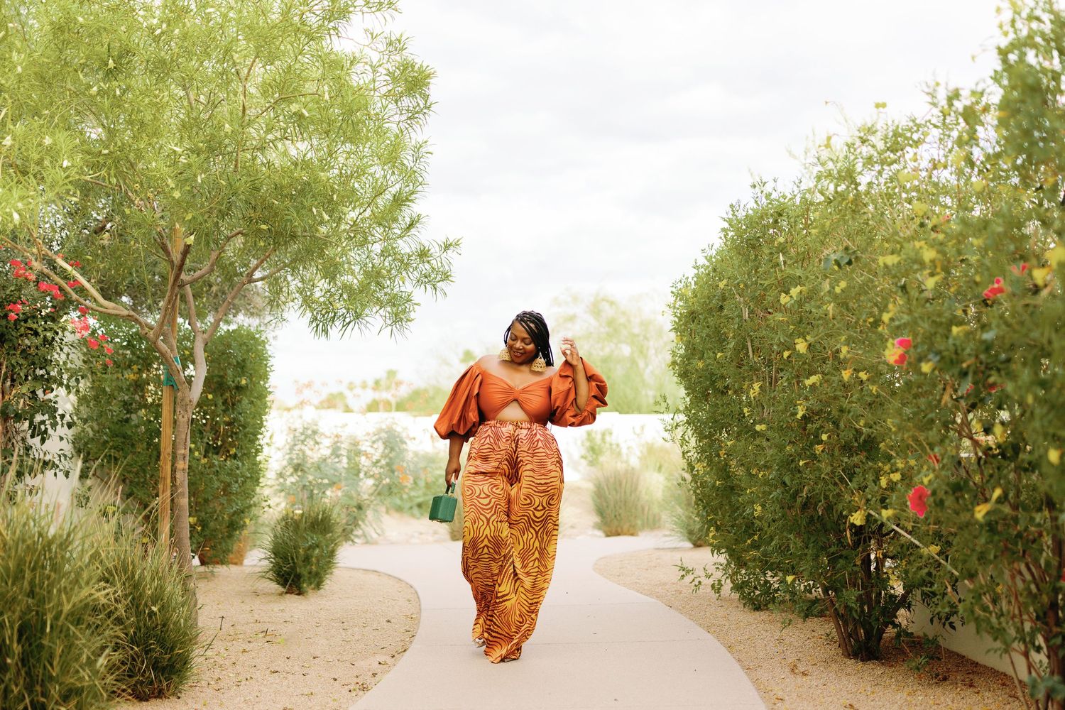 A sequence of images shows someone in a flowy orange dress running and twirling along a dirt path lined with flowering shrubs.