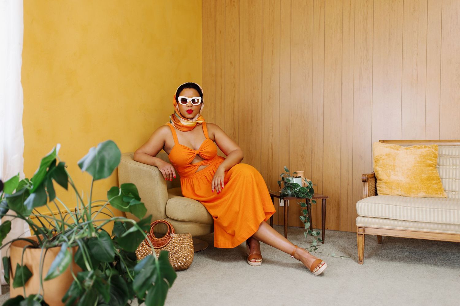Person in vibrant orange outfit lounges in modern interior space with houseplant and minimalist furniture.