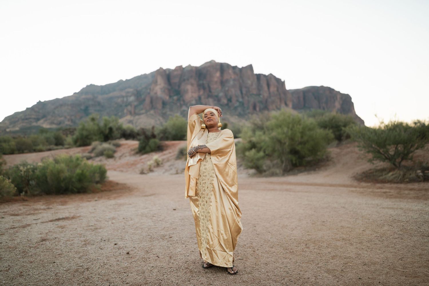 Person in a champagne gold sari dress poses in front of Superstition Mountain in Arizona's desert landscape.