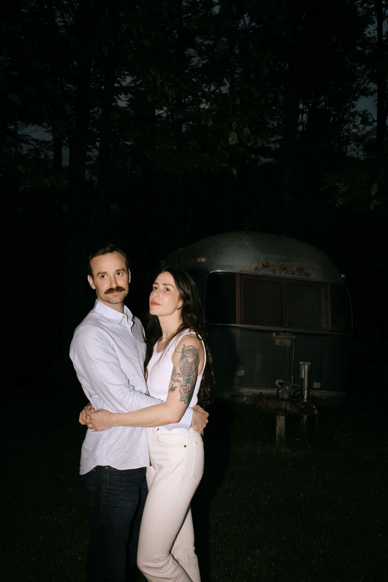 A romantic nighttime embrace outdoors with an antique camper trailer visible in the dark background.