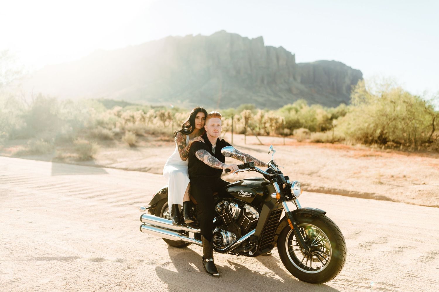 Motorcycle riders enjoying a desert adventure in front of scenic mountain cliffs on a sunny afternoon.
