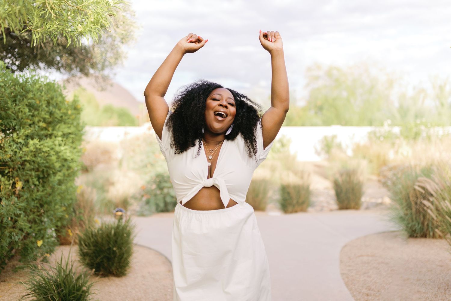 A joyful person in a white dress dances and twirls outdoors during golden hour lighting in a grassy field.