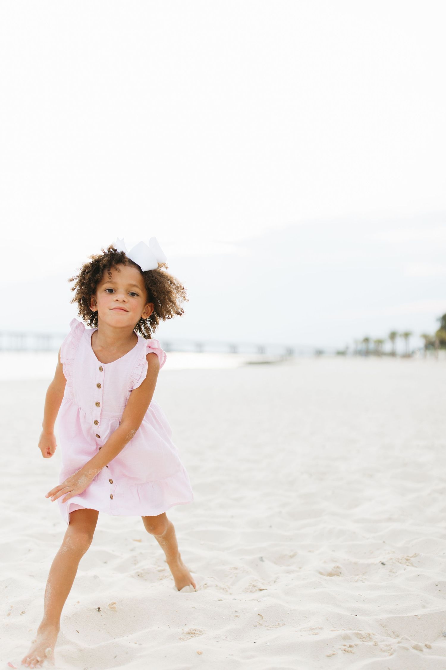 Young child in pink dress plays joyfully on sunny beach.