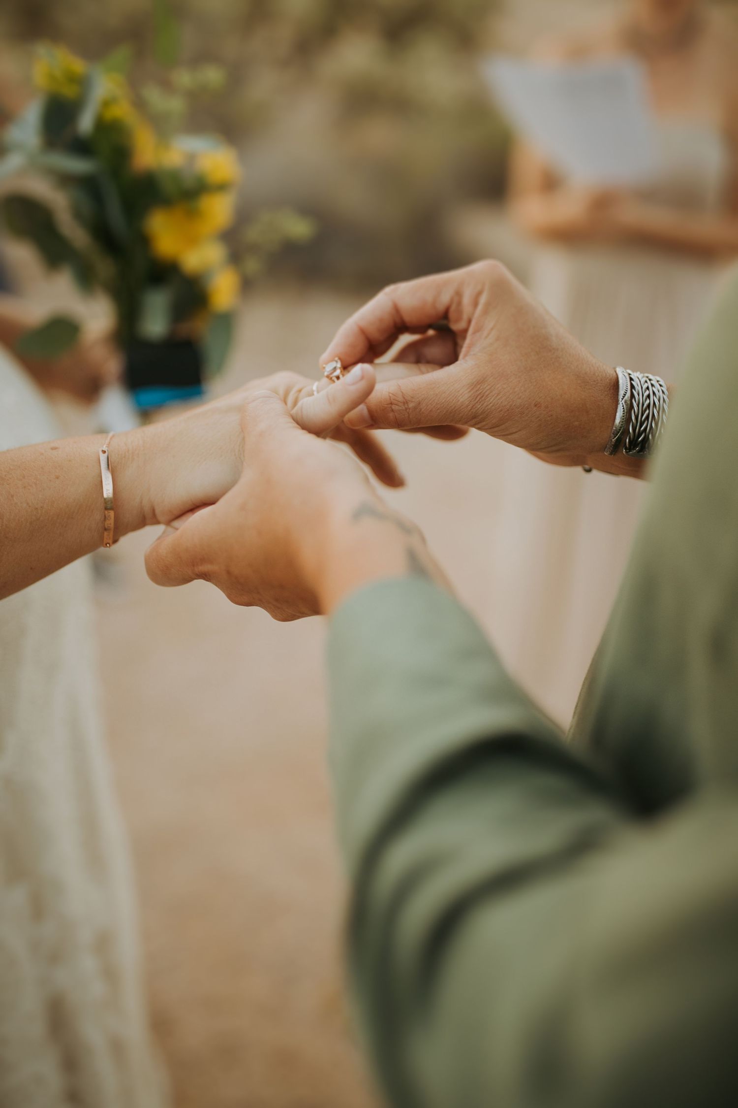 A close-up shot of hands exchanging a wedding ring during a ceremony with yellow flowers in the background.
