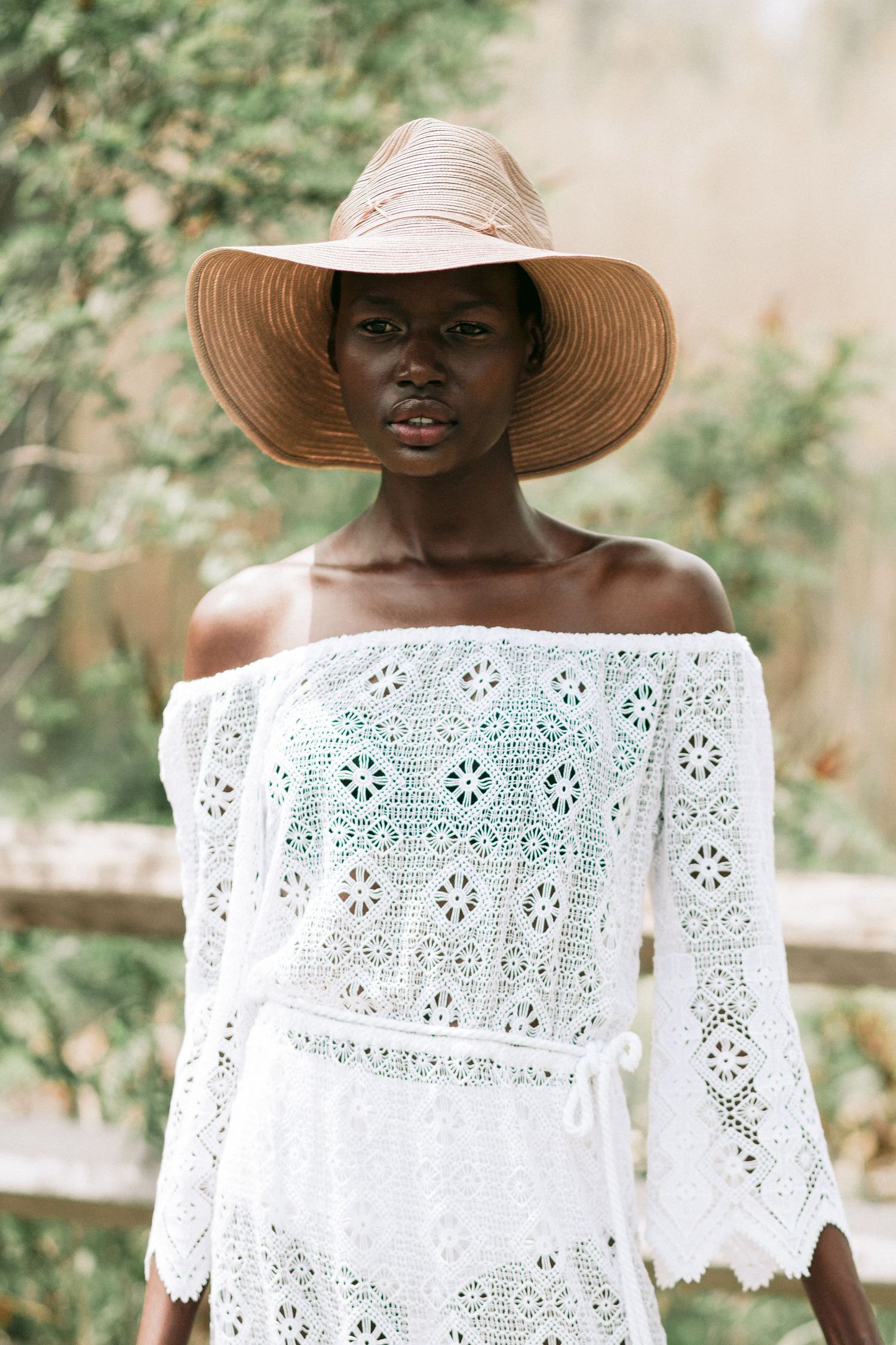 A collage of an off-shoulder white crochet lace top paired with a beige wide-brim sun hat in a natural outdoor setting.