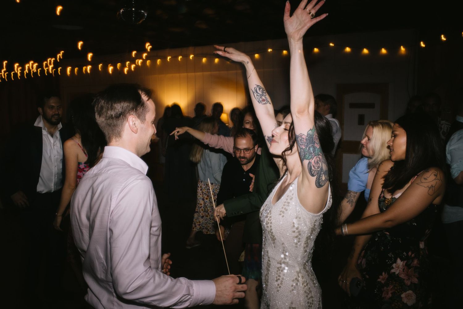Guests dance and celebrate under string lights at an evening wedding reception.