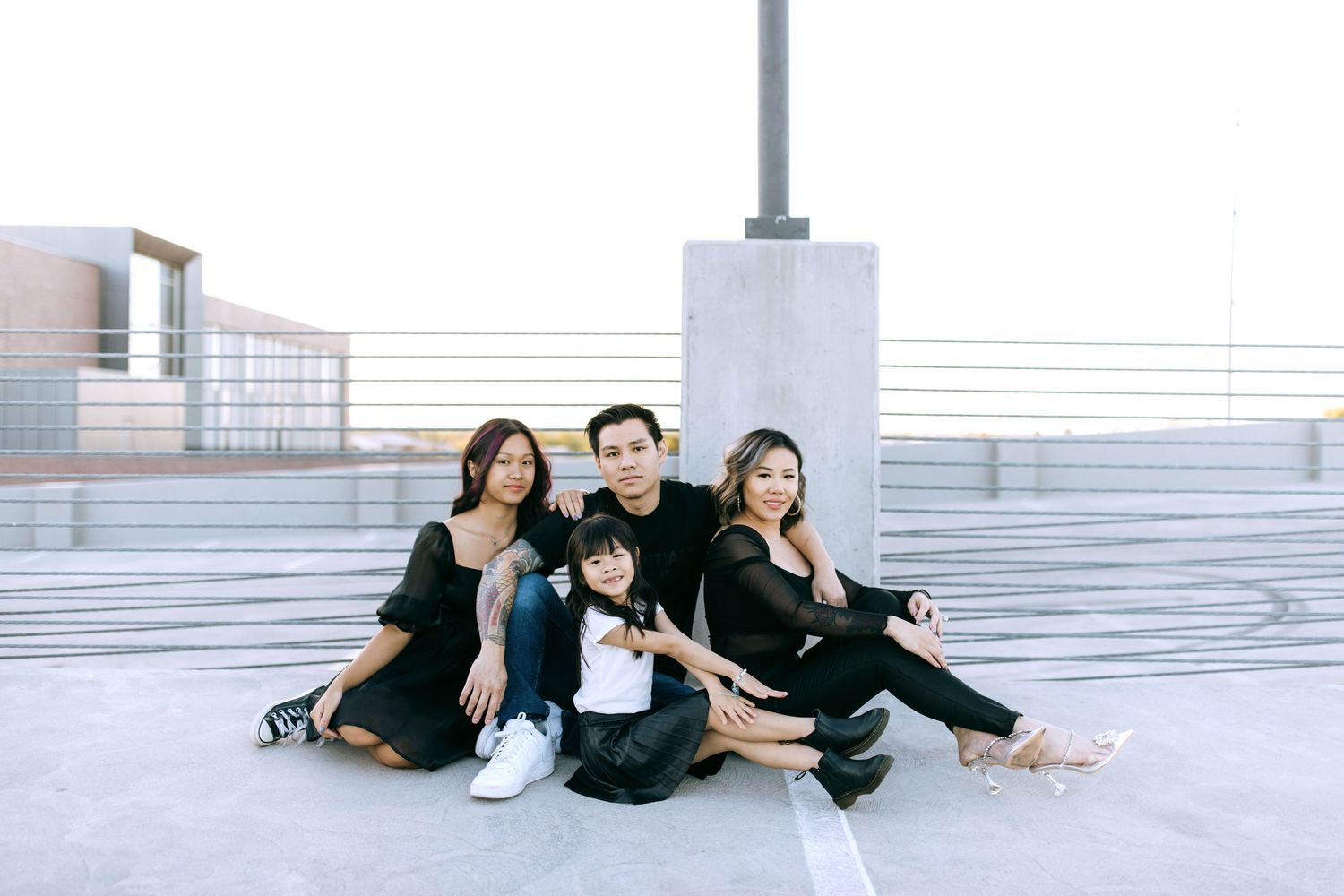 Three friends in black outfits sit casually together on outdoor concrete steps during a photo shoot.