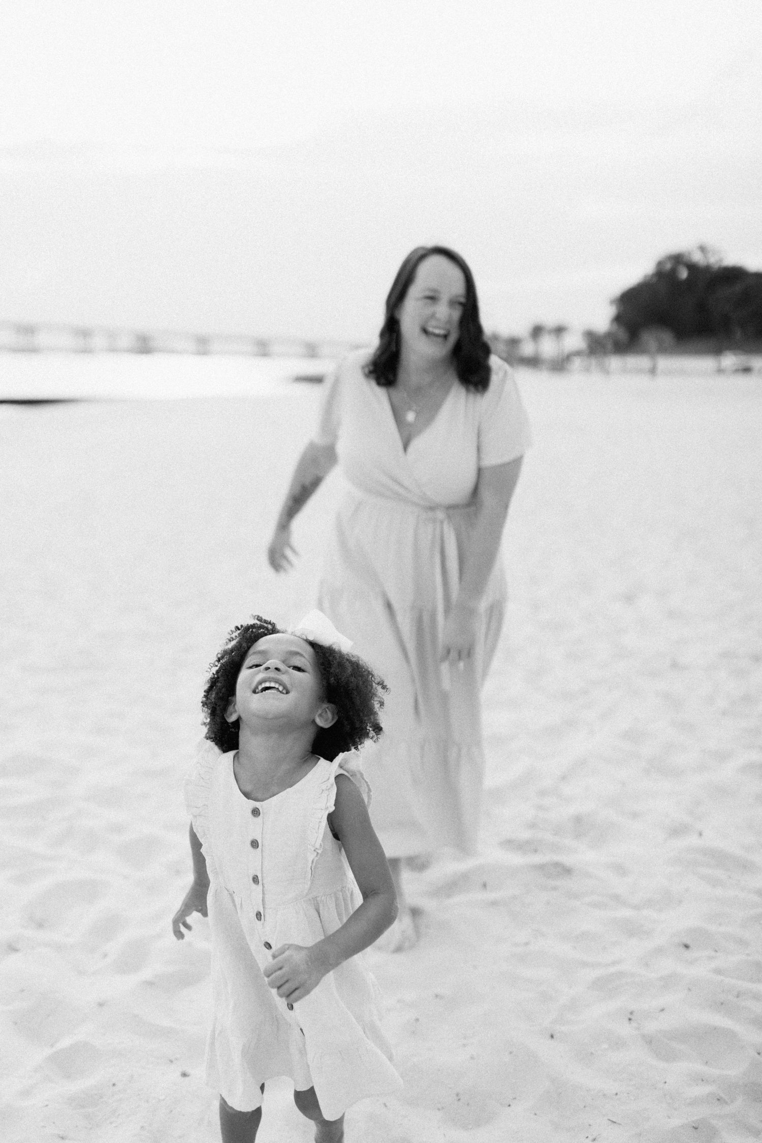 Child in white dress runs and plays freely on pristine beach.