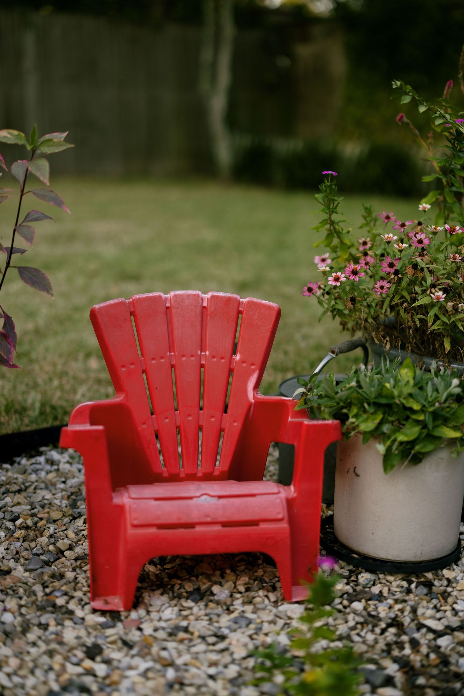 A bright red Adirondack chair sits among landscaping rocks and potted plants in a garden setting.