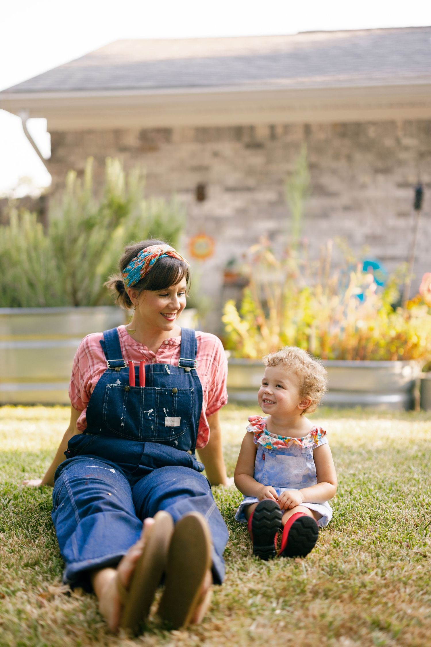 Two people lying in grass outside while wearing blue overalls and sharing a joyful moment together.