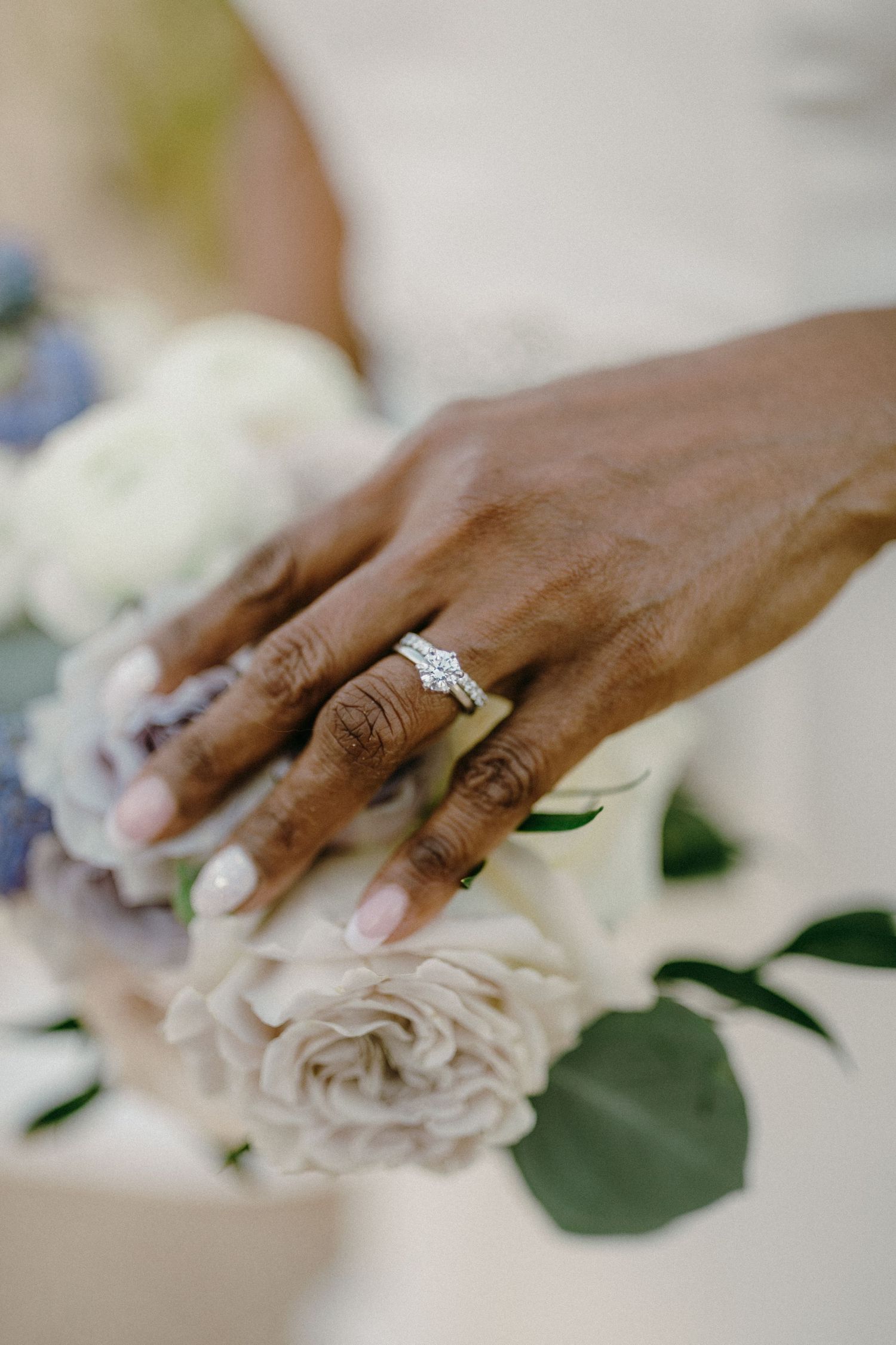 Close-up shot of engagement rings on hands arranging white roses and greenery for wedding decoration.