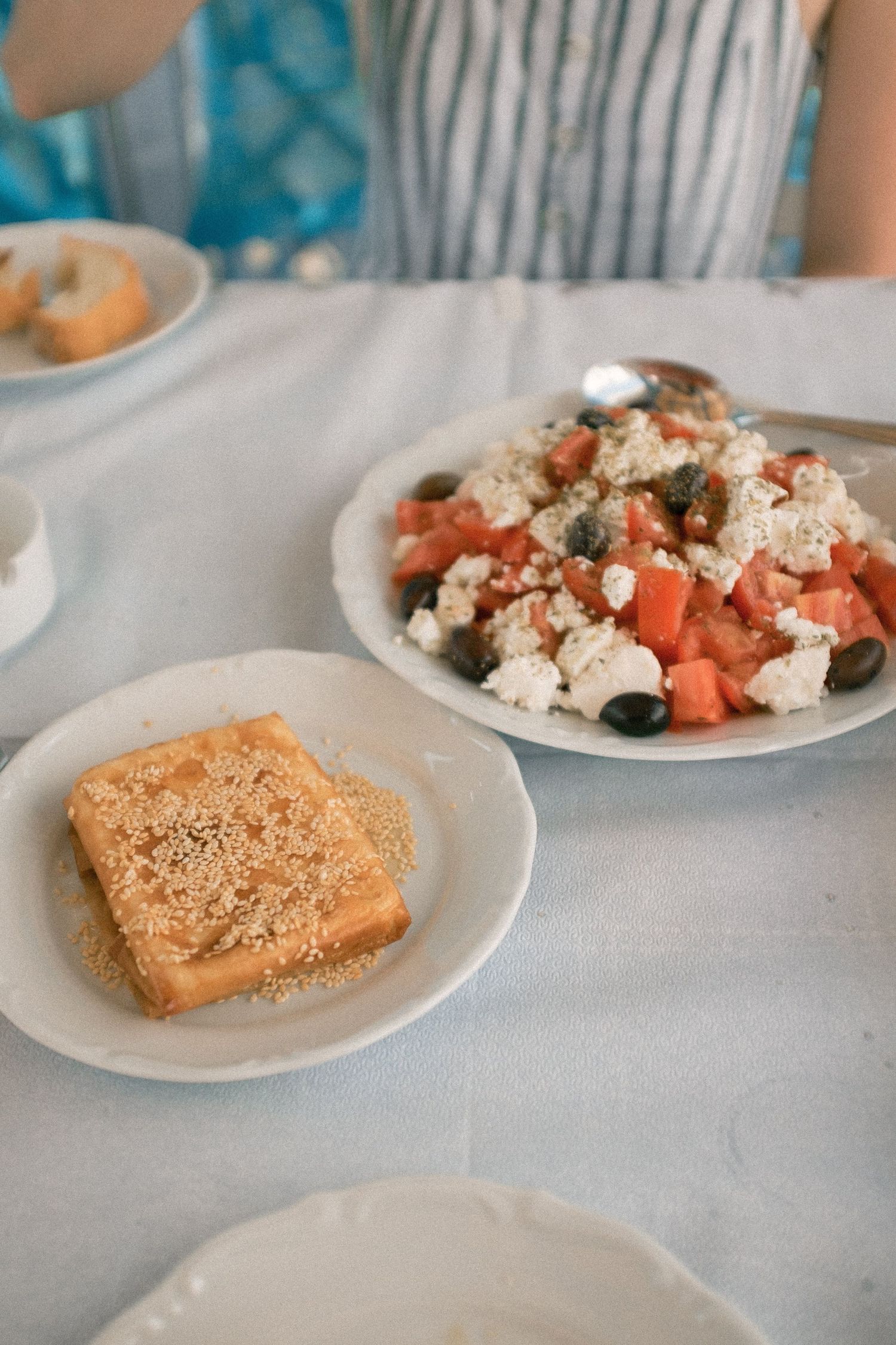 Mediterranean lunch spread with sliced toast and a colorful salad of tomatoes, feta cheese, and olives on white plates.