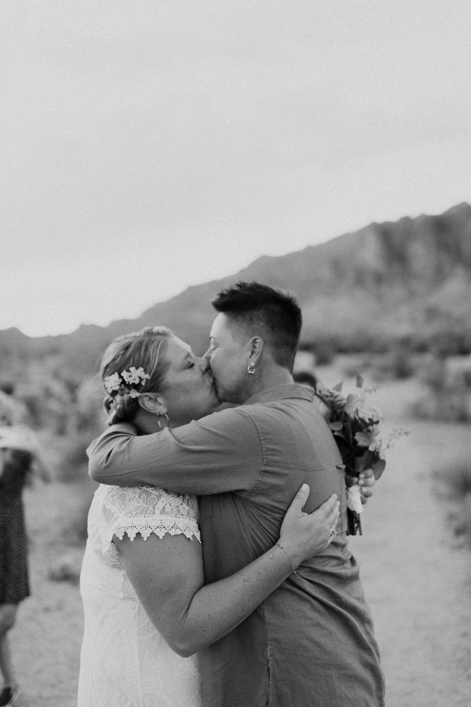 A romantic kiss between newlyweds in a desert landscape captured in three black and white photographs.