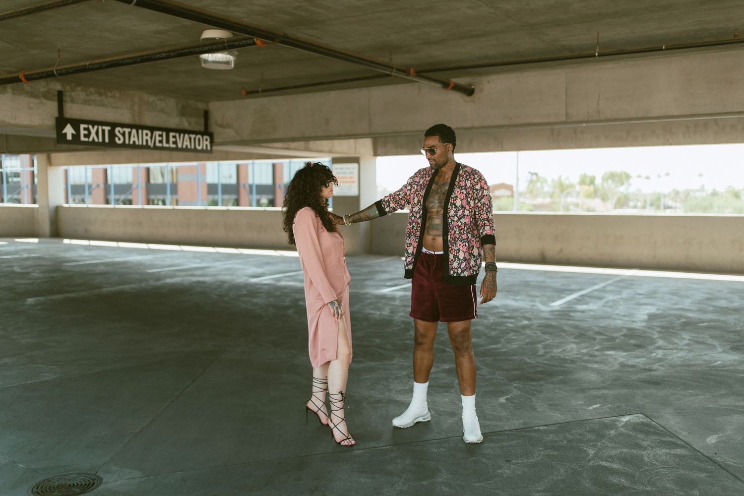 Two people having a conversation in an empty indoor parking garage with concrete walls and floors.