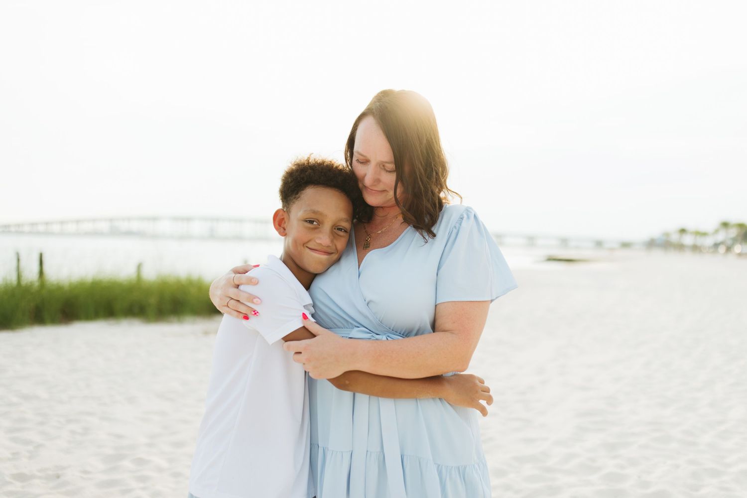 Family members share affectionate embraces while walking together on a sunny beach.