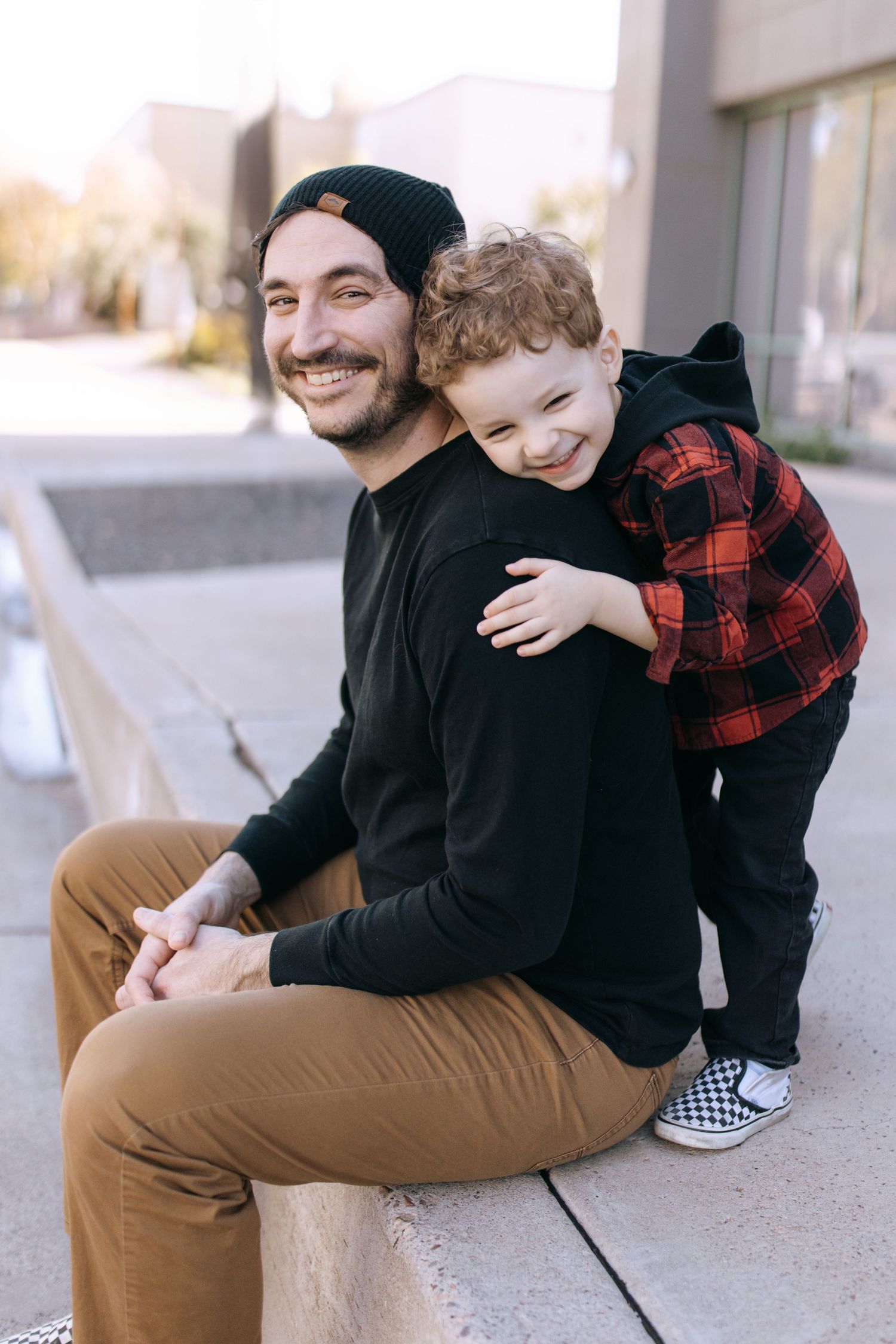 Two people in casual clothing sitting and hugging on concrete ground, showing affection and joy in three similar poses.