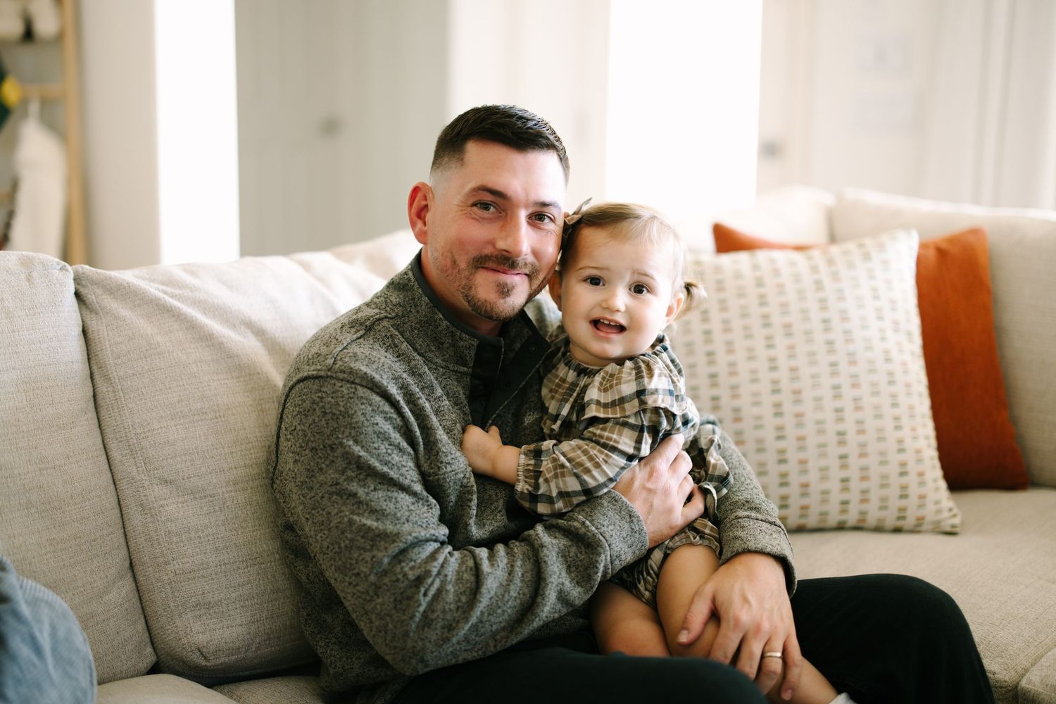 A cozy moment shared between parent and child sitting on a grey couch in a bright, modern living room.