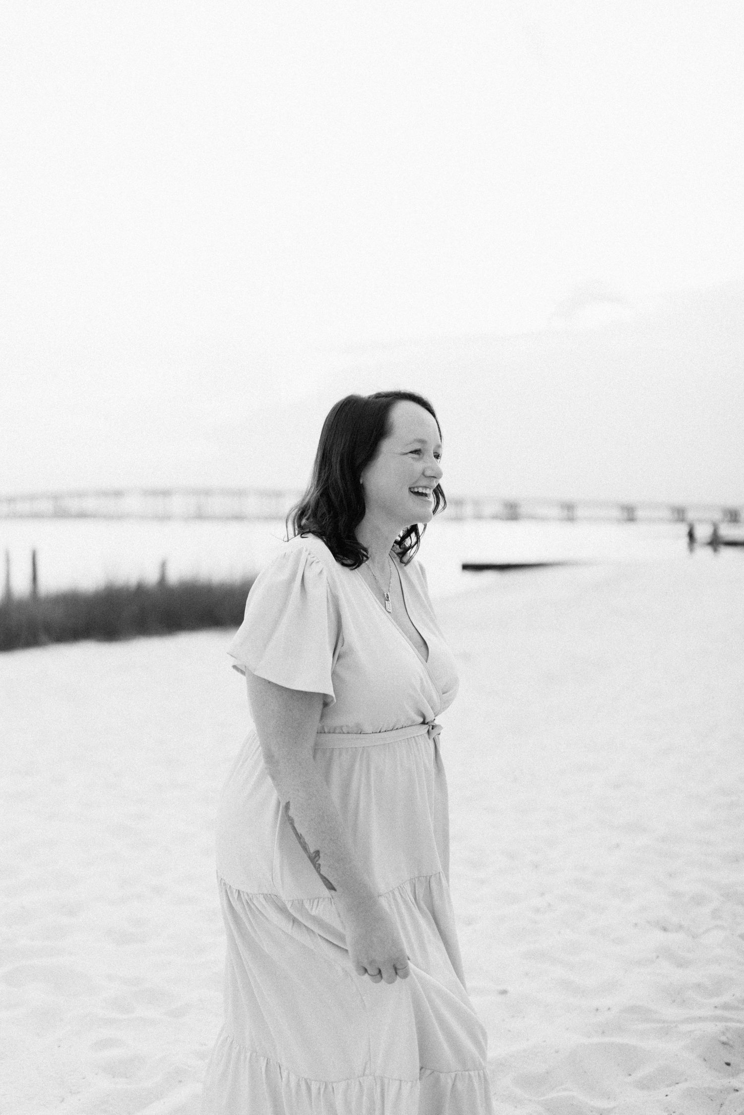 A person in white clothing stands at the beach while laughing, shown in three sequential candid shots.