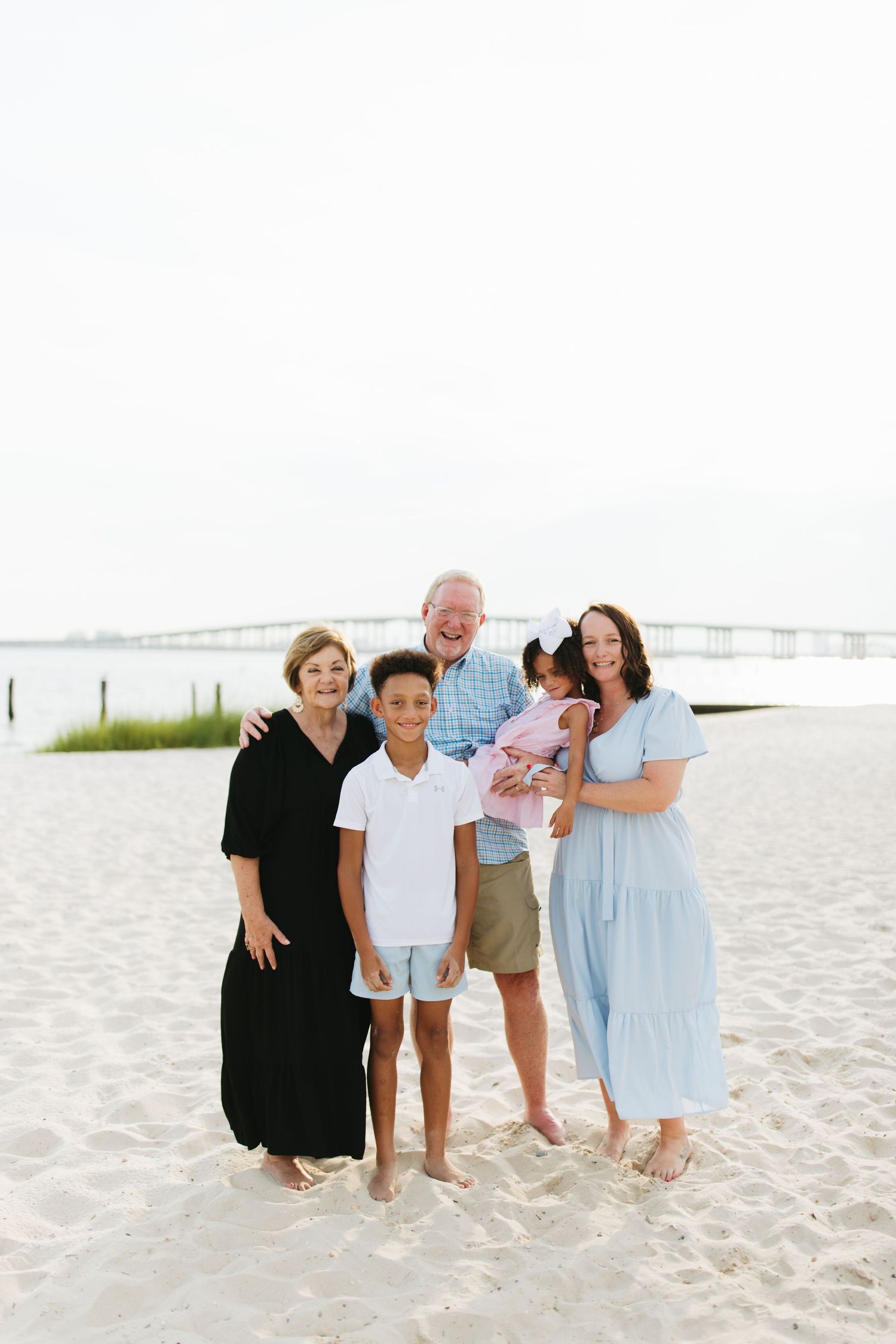 Family members gathered on a pristine beach with coastal vegetation visible in the distance.