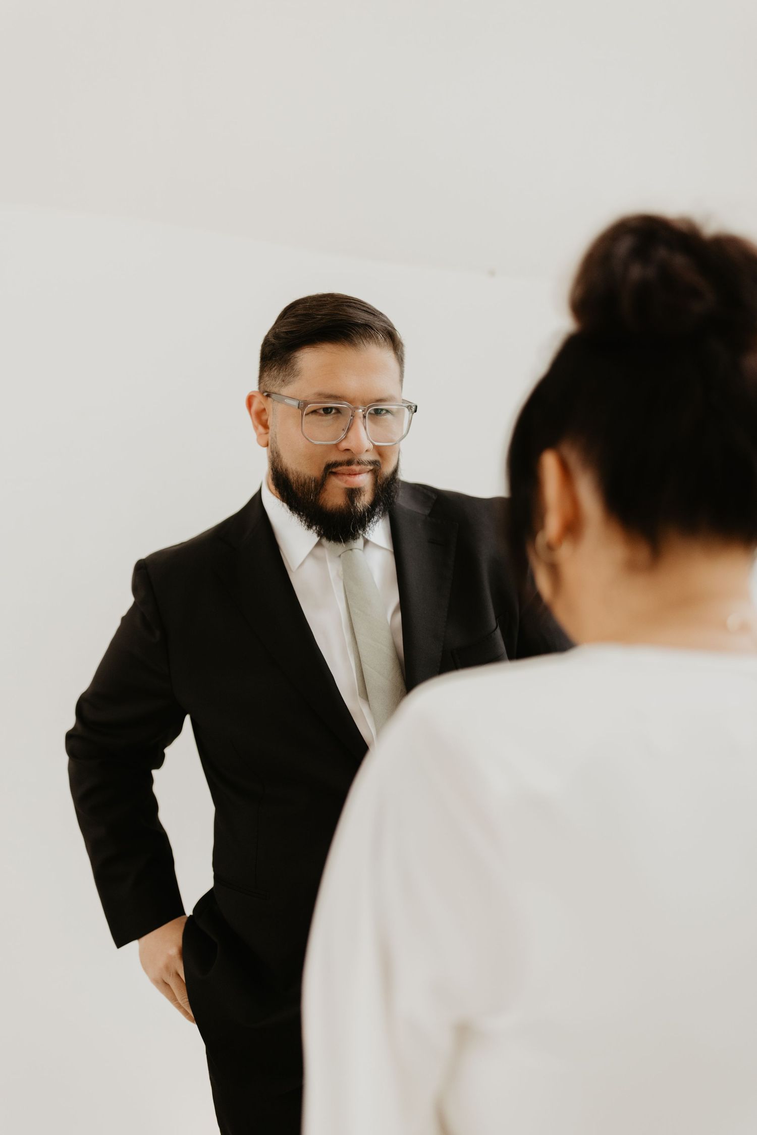 Professional in a black suit and glasses leans into frame as part of a minimalist studio photo sequence.
