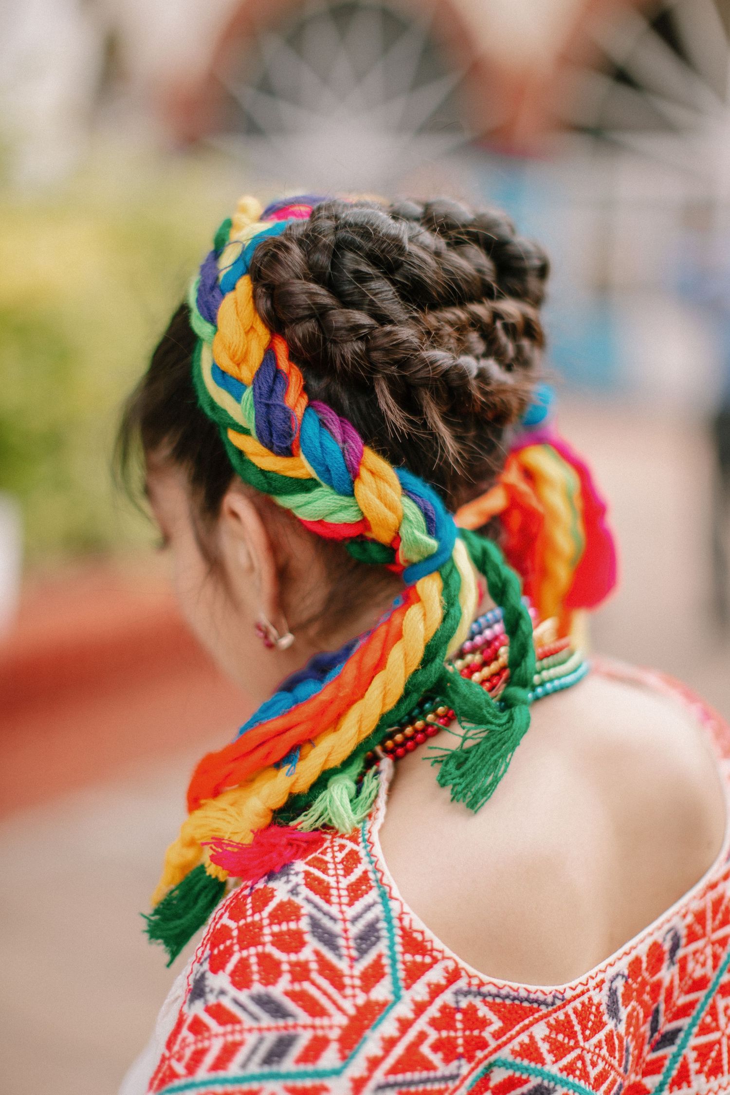 Colorful rainbow braided hair extensions woven into dark hair, paired with a red and white geometric patterned dress.