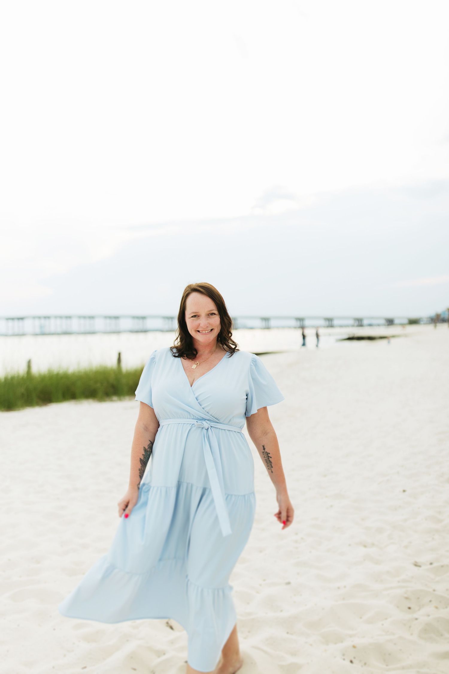Woman in light blue dress twirling joyfully on a sunny beach.