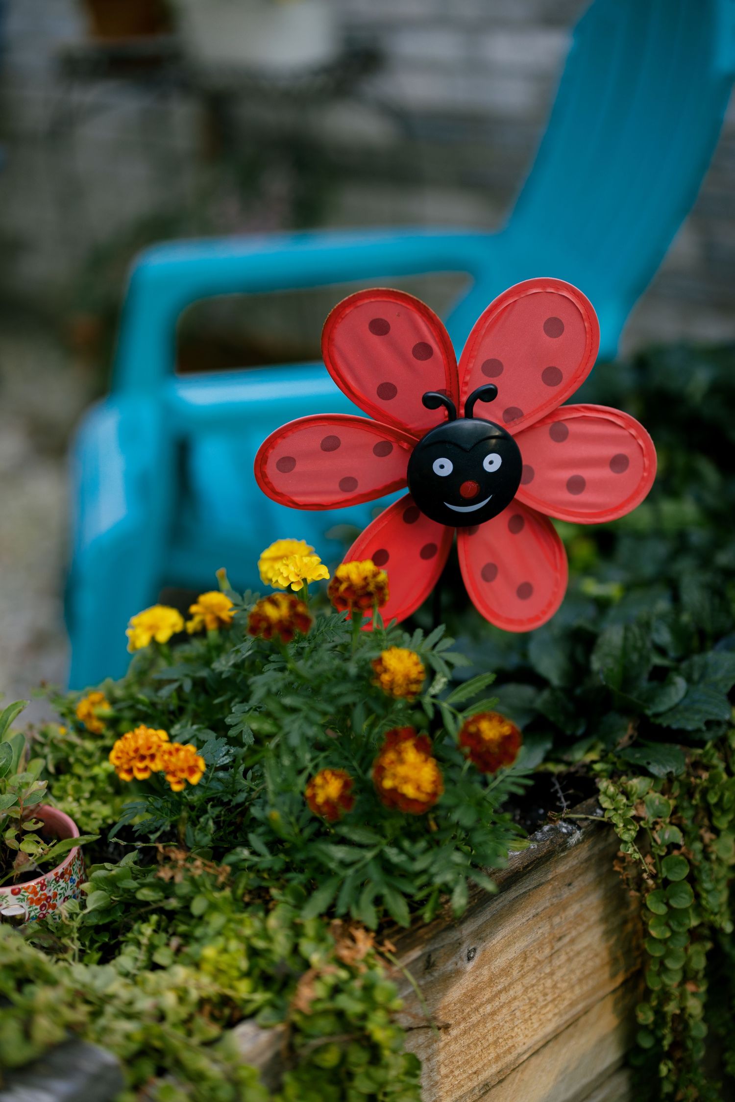 Cheerful red ladybug garden decoration among yellow marigolds in a wooden planter box.